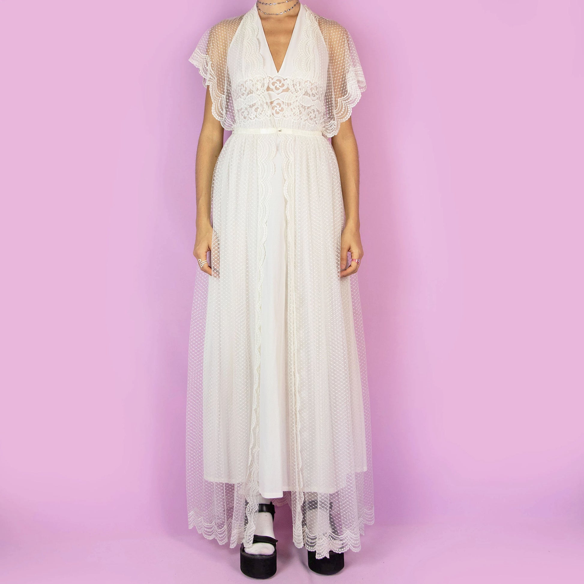 The Vintage 90s White Sheer Duster is a dreamy and ethereal robe, featuring a sheer polka-dot overlay with delicate lace detailing along the edges. The flowy silhouette, flutter sleeves, and maxi length add a romantic charm. Perfect as a layering piece over dresses or casual outfits. Great vintage condition.