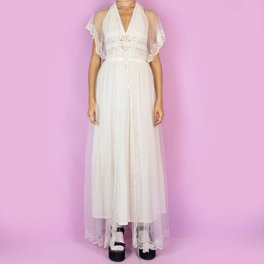 The Vintage 90s White Sheer Duster is a dreamy and ethereal robe, featuring a sheer polka-dot overlay with delicate lace detailing along the edges. The flowy silhouette, flutter sleeves, and maxi length add a romantic charm. Perfect as a layering piece over dresses or casual outfits. Great vintage condition.