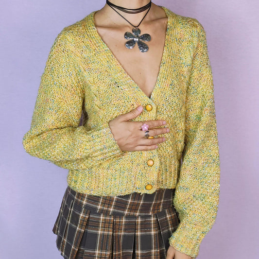 The Vintage 90s Yellow Knit Cardigan is a cozy and vibrant sweater featuring a chunky knit design in a cheerful yellow hue with flecks of multicolored yarn for added texture. This cardigan is styled with a V-neckline, button closure, and ribbed hem