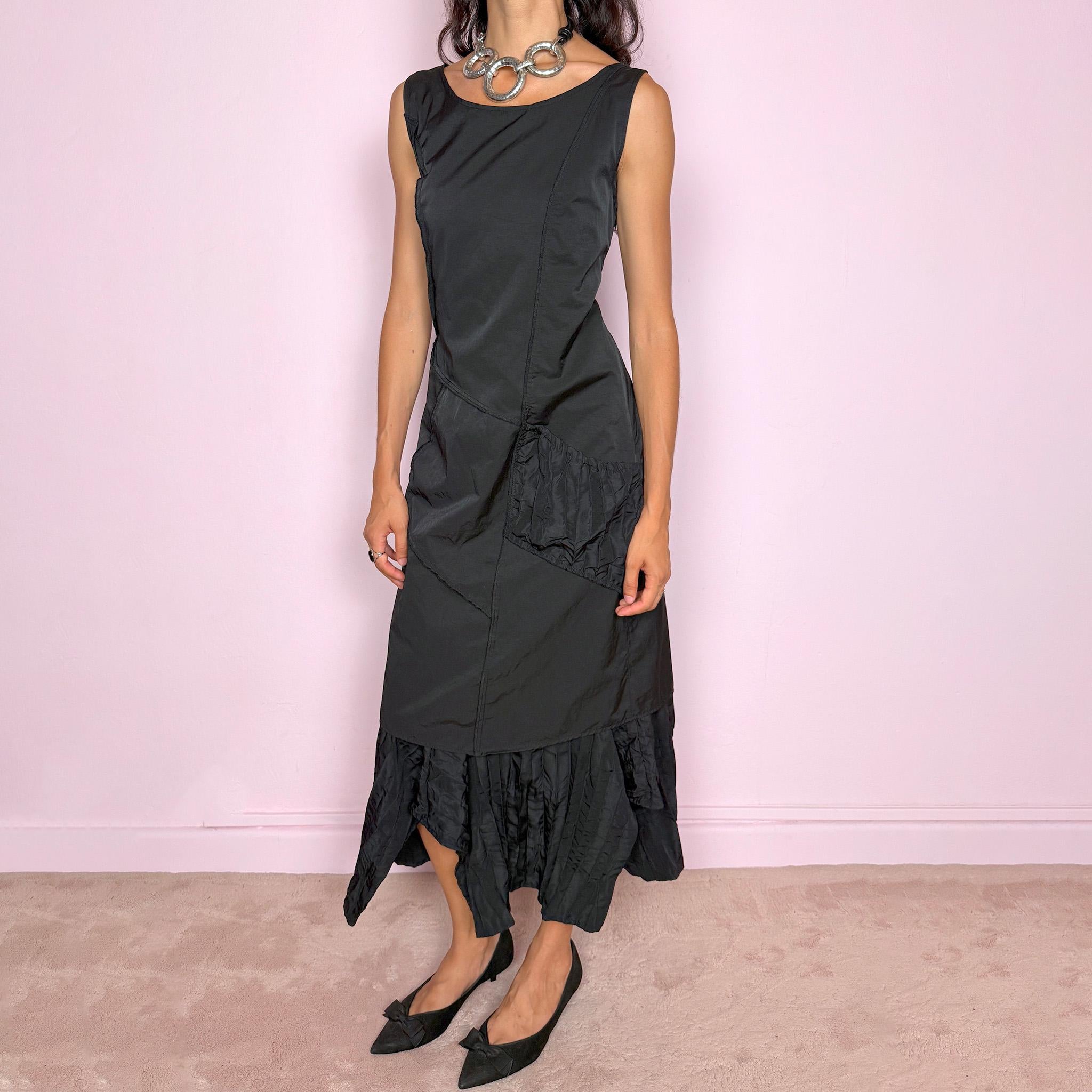 Vintage 2000s black midi dress designed in a structured no-stretch fabric with a side zip closure and an asymmetric panelled silhouette. It features a sleeveless scoop neckline, fitted upper body, diagonal seam construction, and an irregular ruffled hem with crinkled texture for sculptural movement. A dark romantic piece with an understated avant-garde feel, perfect for a minimal gothic look. Made by a French brand from 55% polyamide and 45% cotton, with a 100% polyester lining.
