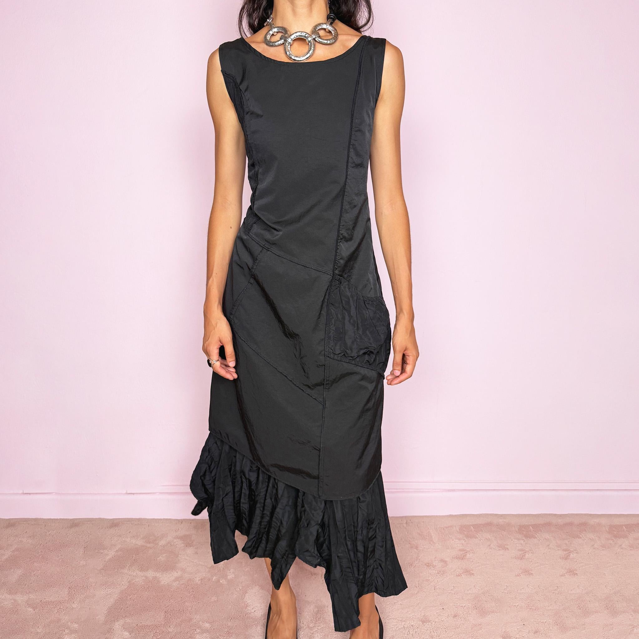 Vintage 2000s black midi dress designed in a structured no-stretch fabric with a side zip closure and an asymmetric panelled silhouette. It features a sleeveless scoop neckline, fitted upper body, diagonal seam construction, and an irregular ruffled hem with crinkled texture for sculptural movement. A dark romantic piece with an understated avant-garde feel, perfect for a minimal gothic look. Made by a French brand from 55% polyamide and 45% cotton, with a 100% polyester lining.