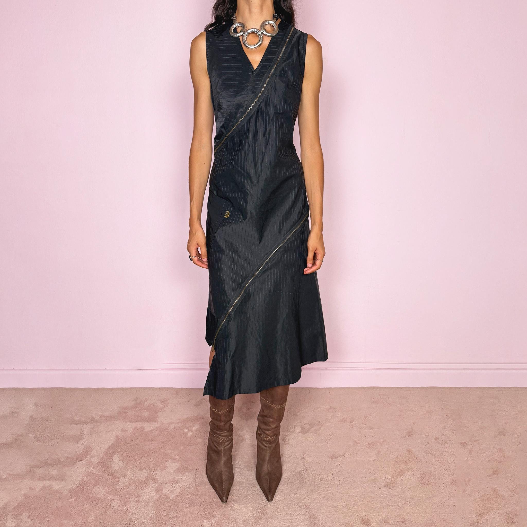 Vintage 2000s black asymmetric midi dress crafted from structured fabric with subtle tonal pinstripes, featuring a fitted sleeveless silhouette, deep V-neckline, and dramatic diagonal exposed zip detailing running across the body. Sculptural asymmetric panel construction creates a deconstructed, avant-garde silhouette with a dark utilitarian feel. Features a side zip closure and no stretch. Made in France by a French brand from 68% cotton and 32% polyamide. Excellent vintage condition.