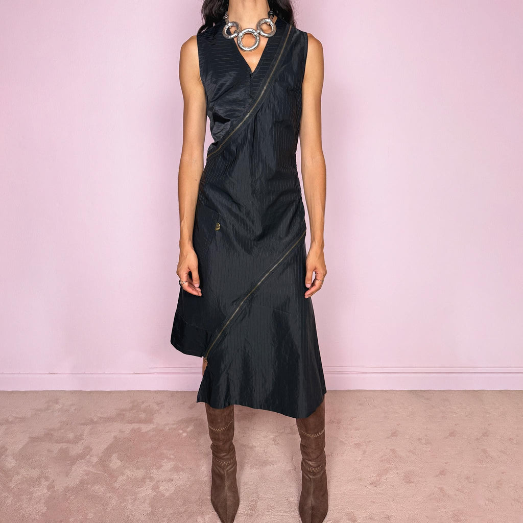 Vintage 2000s black asymmetric midi dress crafted from structured fabric with subtle tonal pinstripes, featuring a fitted sleeveless silhouette, deep V-neckline, and dramatic diagonal exposed zip detailing running across the body. Sculptural asymmetric panel construction creates a deconstructed, avant-garde silhouette with a dark utilitarian feel. Features a side zip closure and no stretch. Made in France by a French brand from 68% cotton and 32% polyamide. Excellent vintage condition.