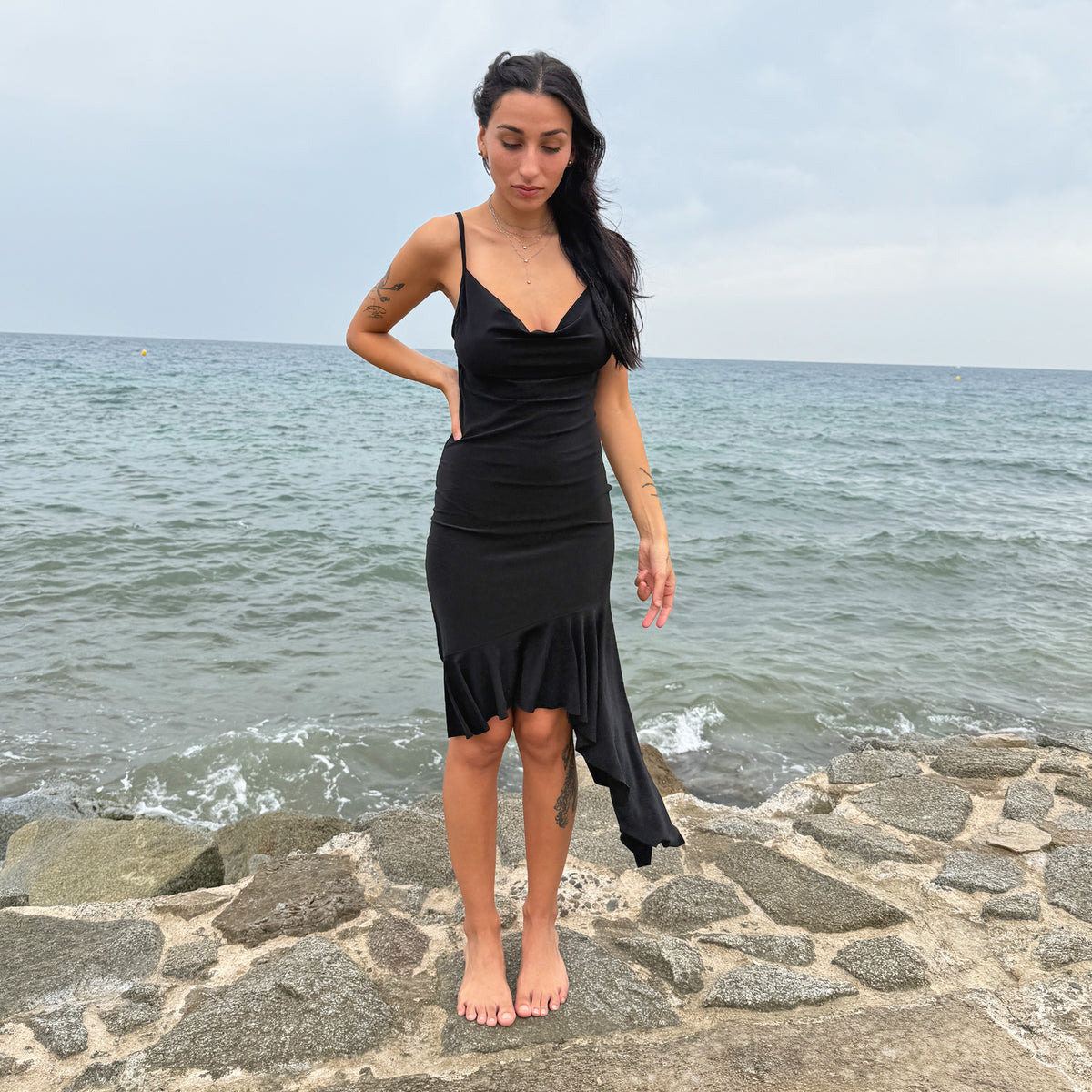 Vintage 2000s black midi dress featuring a plunging cowl neckline, slim spaghetti straps and a fitted body-skimming silhouette. Finished with a dramatic asymmetric ruffled hem that falls into an elongated cascading side panel. Made by a French brand from a stretchy polyester blend. Great vintage condition.