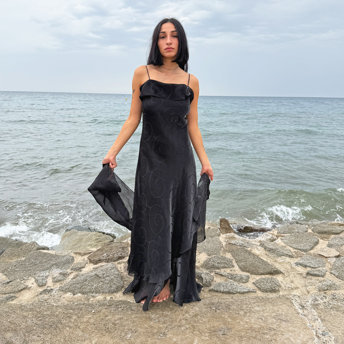 Vintage 2000s statement black maxi dress with an iridescent shimmer and elegant layered construction. Features spaghetti straps, an asymmetrical tiered hem, a sheer overlay with a swirl pattern, and a matching fabric scarf. Non-stretch. Perfect for evening events or occasionwear. Made in France. Main fabric: 78% viscose and 22% polyester; lining: 100% polyester. Excellent vintage condition.
