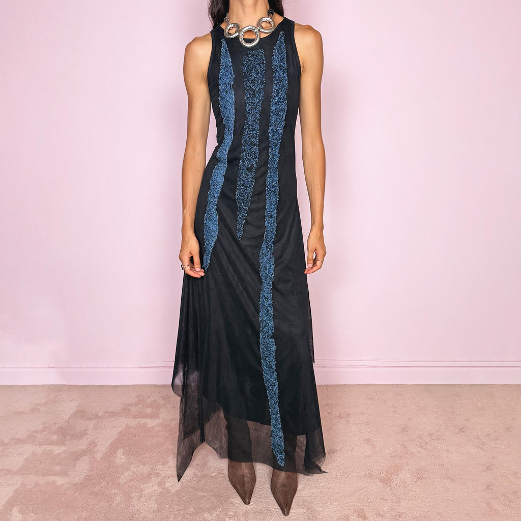 Vintage 2000s maxi dress crafted from stretchy black mesh with a fitted sleeveless silhouette, a semi-sheer outer layer, and an asymmetric flowing hem. Detailed with contrasting blue embroidered threadwork running vertically across the body, creating a textured effect with a distinctly avant-garde Y2K feel. Made in Italy by an Italian brand from 100% polyamide. Excellent vintage condition.