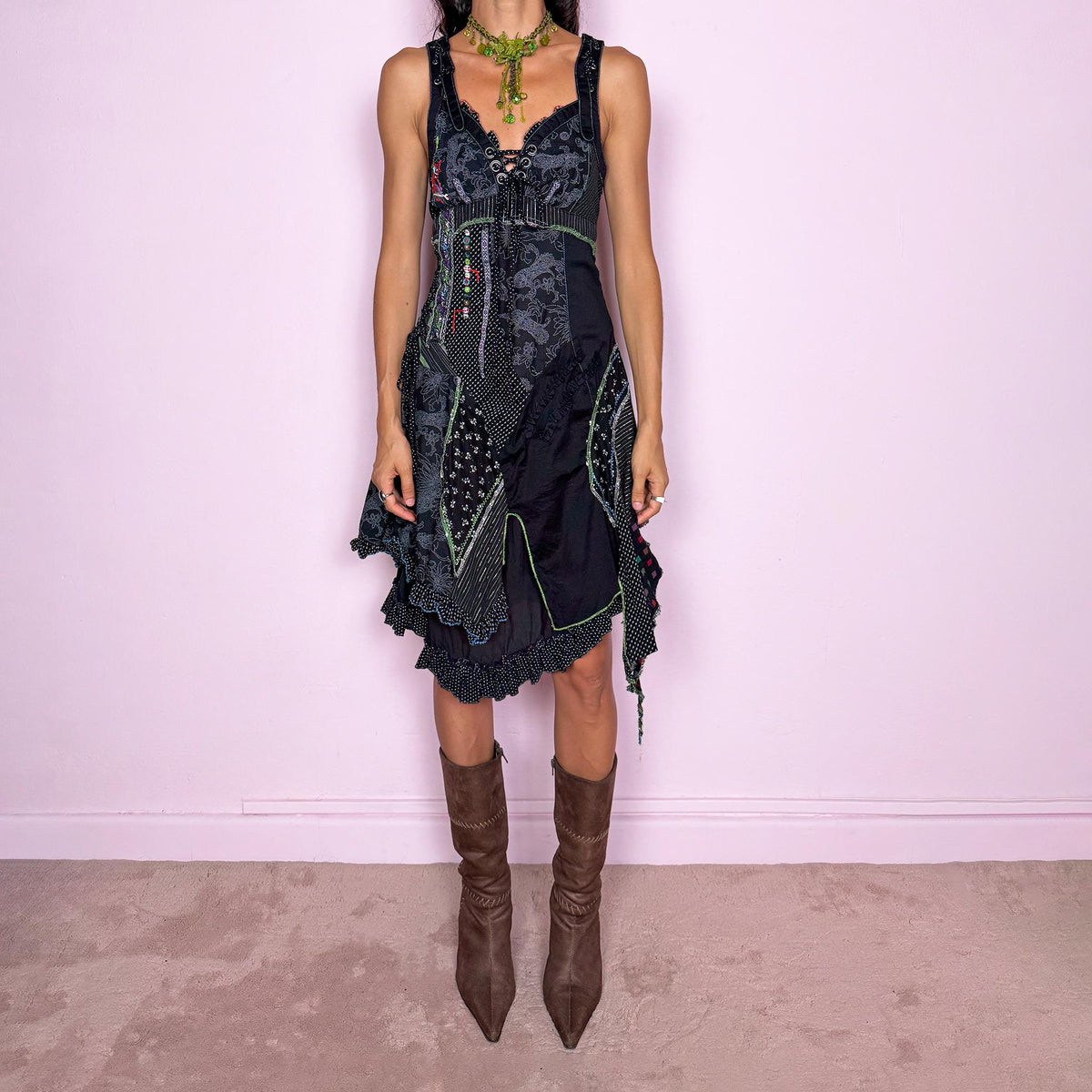Vintage 2000s black midi dress featuring a deconstructed patchwork construction with mixed pinstripe, floral, and textured panels. Designed with a deep lace-up neckline, asymmetric layered skirt, raw-edge detailing, decorative stitching, and a dramatic draped side panel. Finished with a side zip closure. Non-stretch. The irregular construction and mixed textures are ideal for ragged-doll, avant-garde looks.