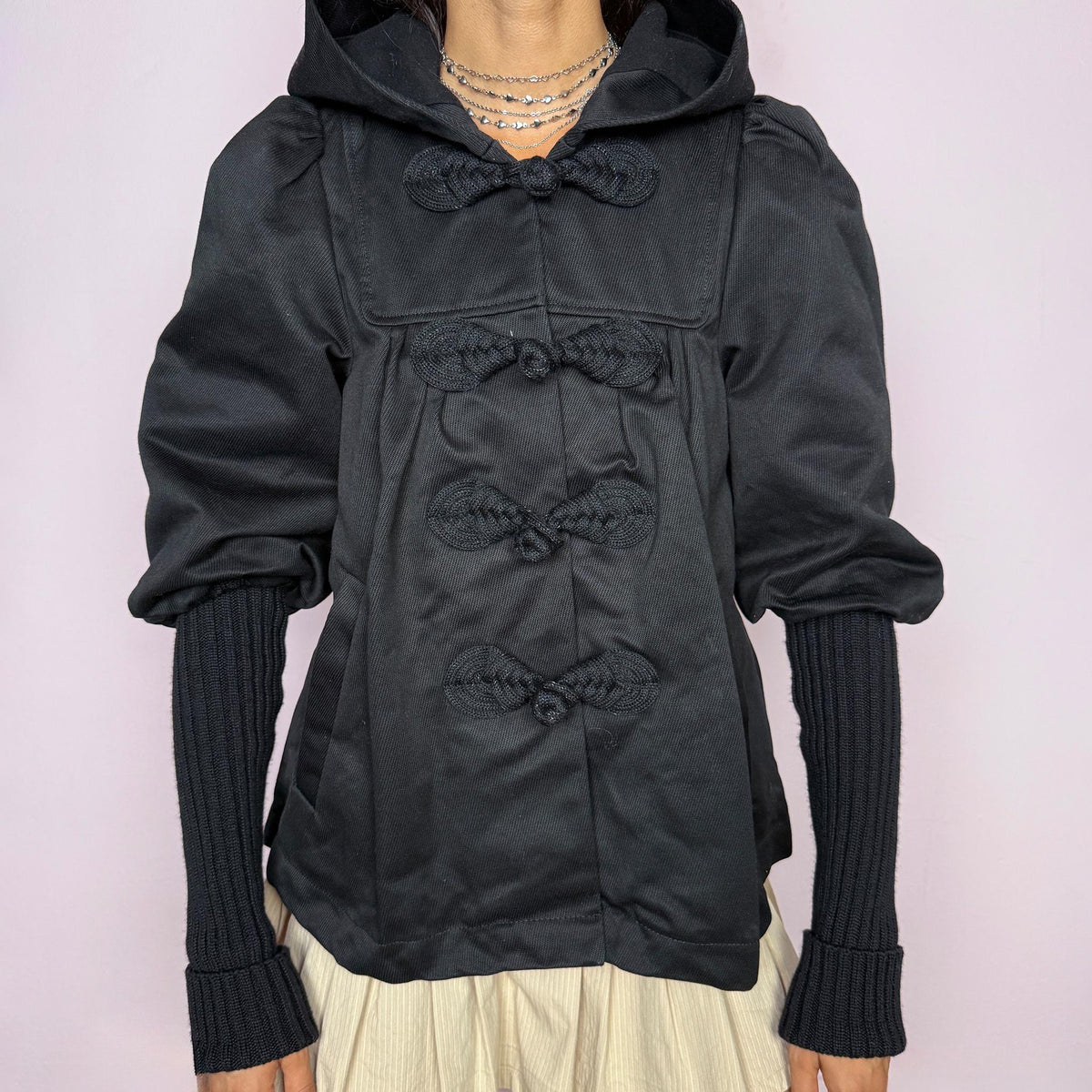 Vintage 2000s black hooded jacket featuring a structured silhouette with a hood, braided frog-style front closures, puffed sleeves, extra-long ribbed knit cuffs, and front pockets. A statement piece for dark avant-garde looks. Non-stretch. From an Italian brand, crafted from 100% cotton with a lining of 51% polyester, 34% viscose, 13% acetate, and 2% spandex. Excellent vintage condition.