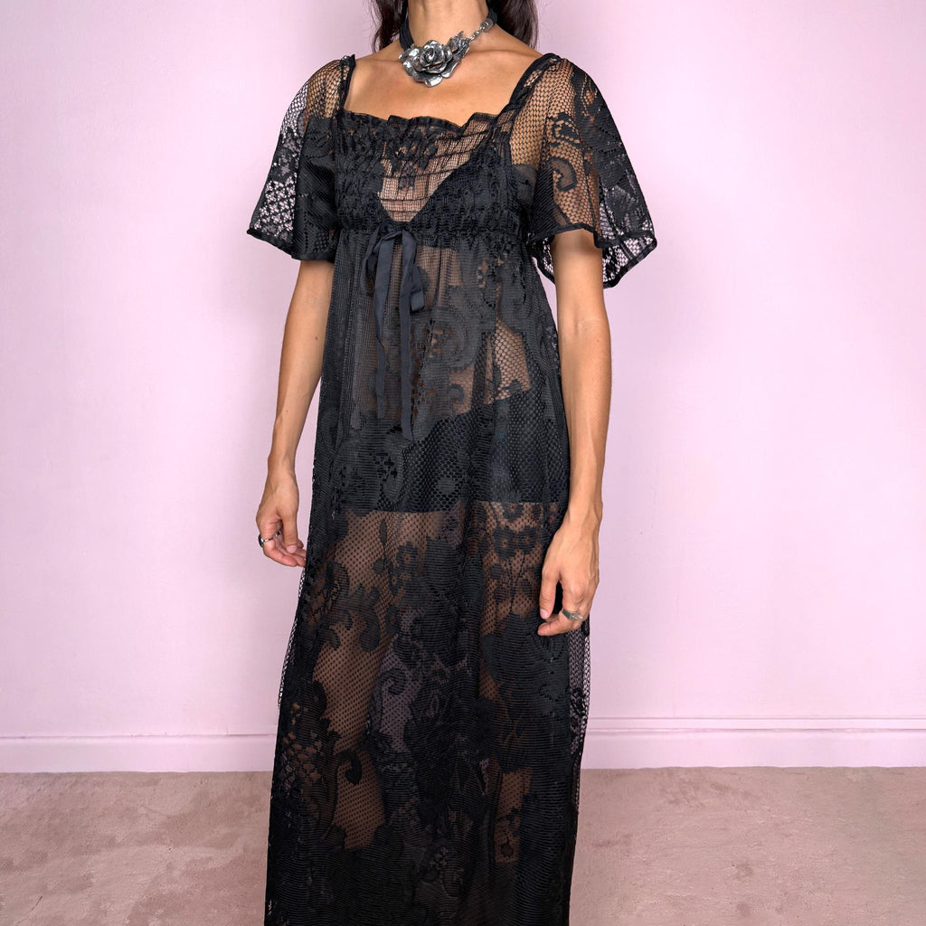 Vintage 90s black sheer lace maxi dress featuring an intricate all-over lace design with mixed floral and geometric motifs. Designed with a square neckline, softly gathered bust, short sheer sleeves, front tie detail, and a relaxed floor-length silhouette with a semi-sheer lining. For dark romantic styling and layered looks. The labels are missing, so the exact fabric is unknown. Excellent vintage condition.