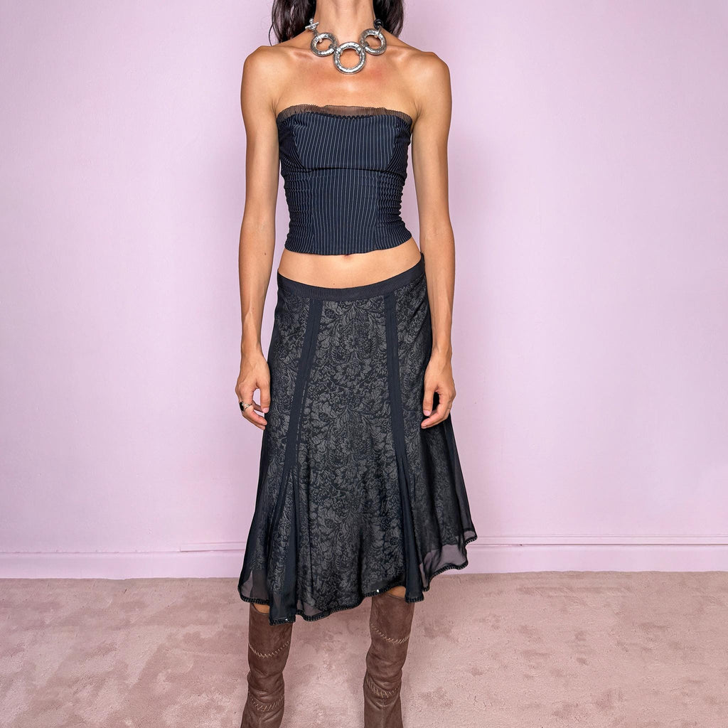 Vintage 2000s black silk A-line flared midi skirt crafted from 100% silk, with contrasting beige and black lining that subtly reveals an intricate dark floral paisley pattern through the outer fabric, a semi-sheer black overlay, and delicate black sequin trim along the edge. Elegant with a romantic eveningwear feel. Non-stretch with a side zip closure. Can be worn mid-rise for size M or lower-rise for size S. From a German brand. Excellent vintage condition.