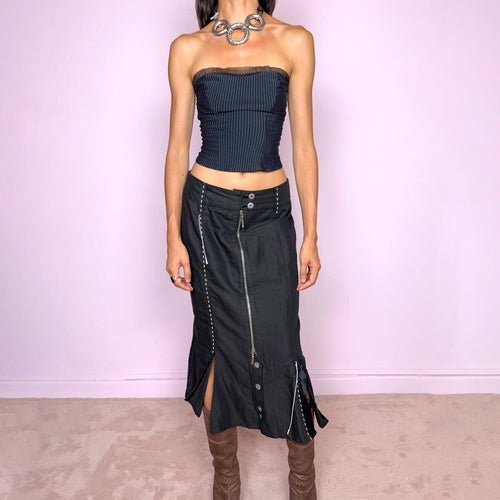 Vintage 2000s black midi skirt featuring an exposed full-length front zip, double-button waistband, and contrast white stitching throughout. The lower section opens into sculptural deconstructed panels with additional button and zip detailing, creating an asymmetric, utilitarian avant-garde feel. Can be worn high-waisted for size M or slightly lower on the waist for sizes S and XS. Non-stretch. Made in Holland by a Dutch brand from a structured blend of 52% cotton and 48% linen