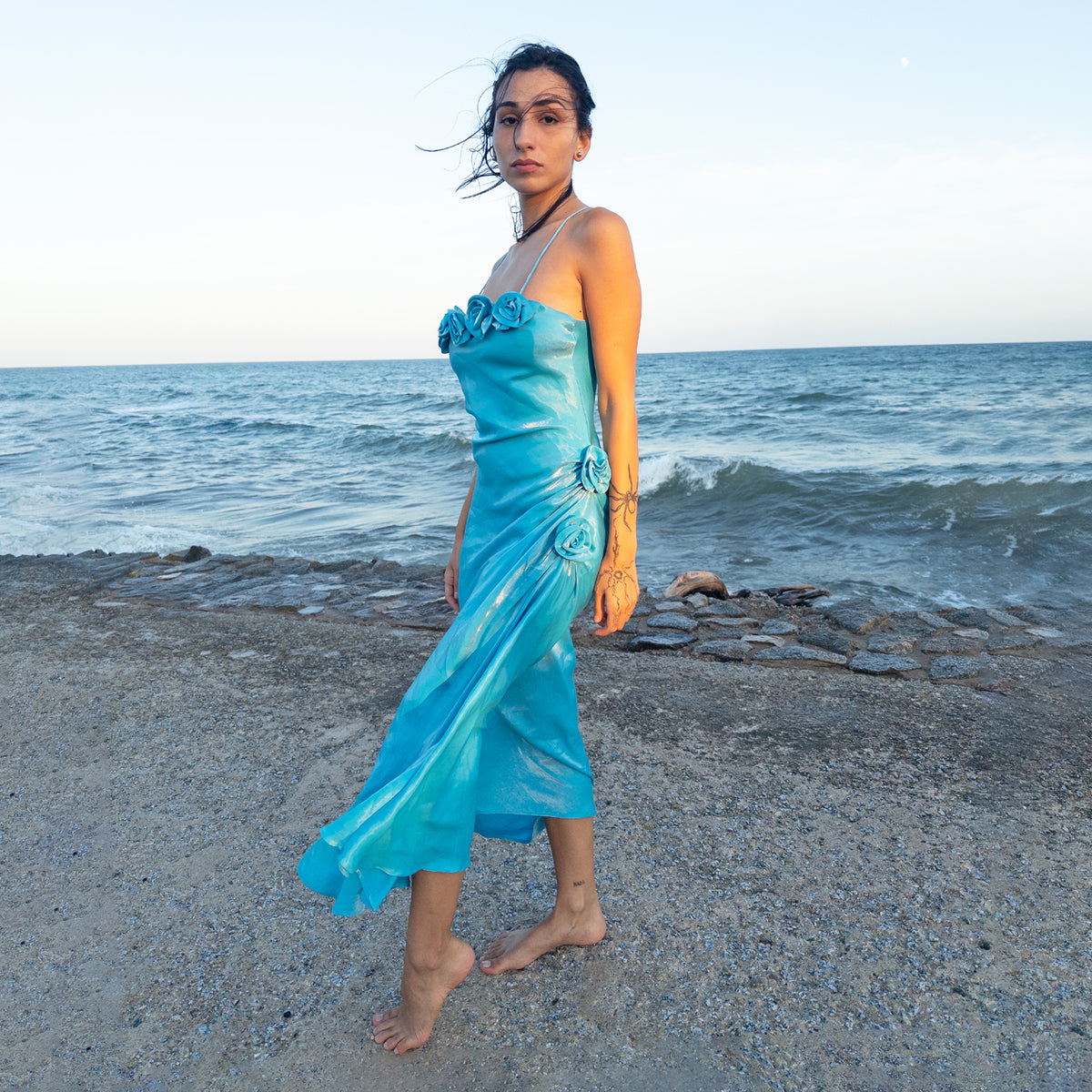 Vintage 2000s blue slip midi dress with a luminous iridescent sheen. Features slim spaghetti straps, sculptural rosette appliqués along the neckline and hip, gathered side ruching, and an asymmetric draped skirt. Perfect for statement occasionwear, summer wedding looks, and dreamy evening styling. Composition label is missing, so the exact fabric is unknown. From a French brand. Great vintage condition.