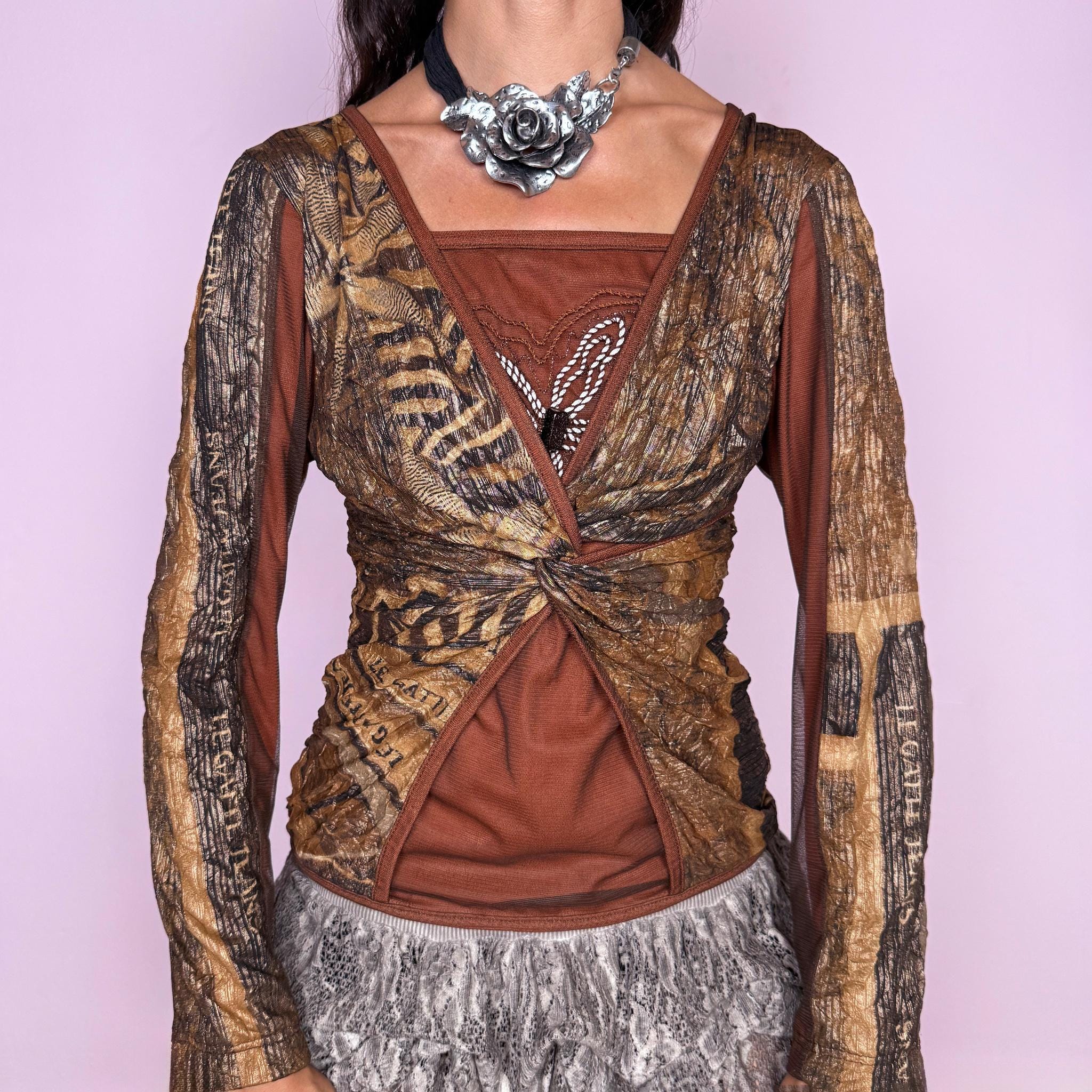 Vintage 2000s layered mesh top featuring a richly textured brown and bronze graphic mesh construction with contrasting panels, a sculptural front twist detail, and gathered mesh layering. Finished with an embroidered motif at the front and long paneled sleeves. A striking deconstructed piece with a distinctly avant-garde Italian maximalist feel. Made in Italy by an Italian brand from stretchy 100% polyester. Excellent vintage condition.