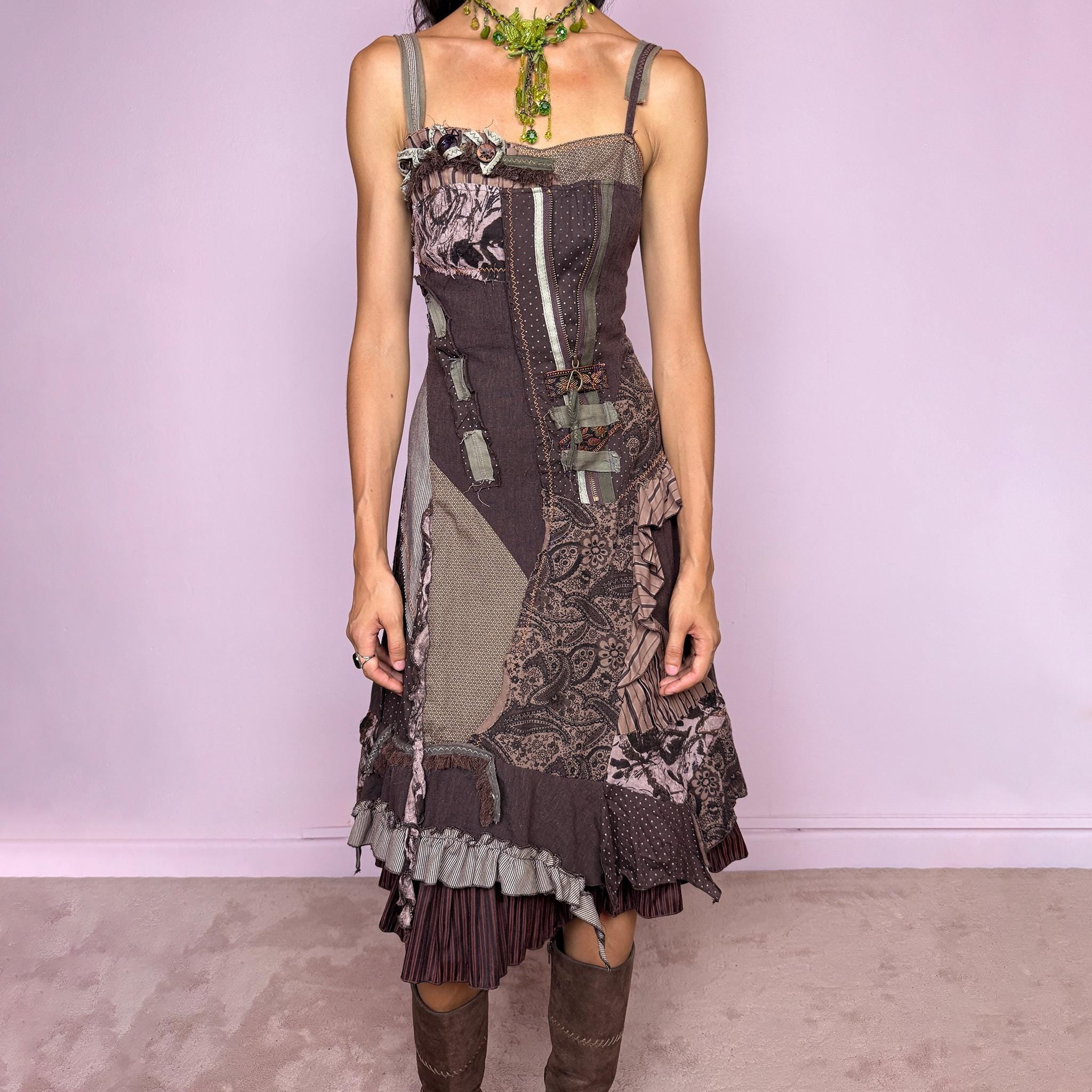 Vintage 2000s deconstructed midi dress with a distinctive rag-doll-inspired patchwork construction in brown, khaki green, mauve, and gray tones. Featuring mixed patterned panels, exposed raw-edge seams, contrast stitching, ribbon and buckle details, gathered ruffles, and an irregular layered hem for a highly textured avant-garde silhouette. Designed with adjustable shoulder straps, a shirred elastic back for flexibility, and a side zip closure.