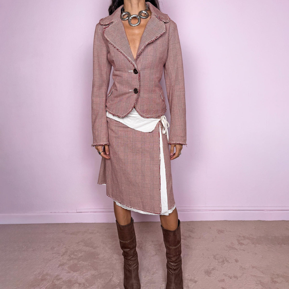 Vintage 2000s burgundy-red and cream two-piece skirt suit. The set includes a fitted blazer with a glen plaid / Prince of Wales check pattern, raw-edge trim, notched lapels, and a two-button front closure. Paired with a matching wrap-style midi skirt featuring layered cream lining, a side button closure, and an adjustable tie. The contrasting construction and unfinished edges create a relaxed, deconstructed feel while maintaining a tailored silhouette.