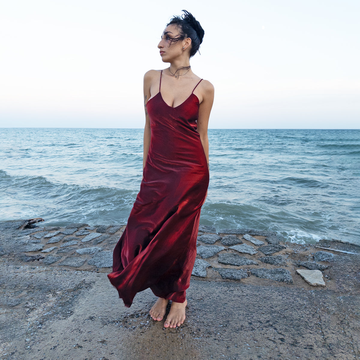 Vintage 2000s burgundy-maroon slip maxi dress made in France by a French brand, featuring a fluid, body-skimming silhouette, slim spaghetti straps, a deep V-neckline, and a subtle iridescent sheen that shifts between deep burgundy and rich red tones in the light. The long, bias-cut shape creates a sleek, sensual drape for evening glamour. Made from a non-stretch blend of 78% viscose and 22% polyester with a 100% polyester lining. Excellent vintage condition.