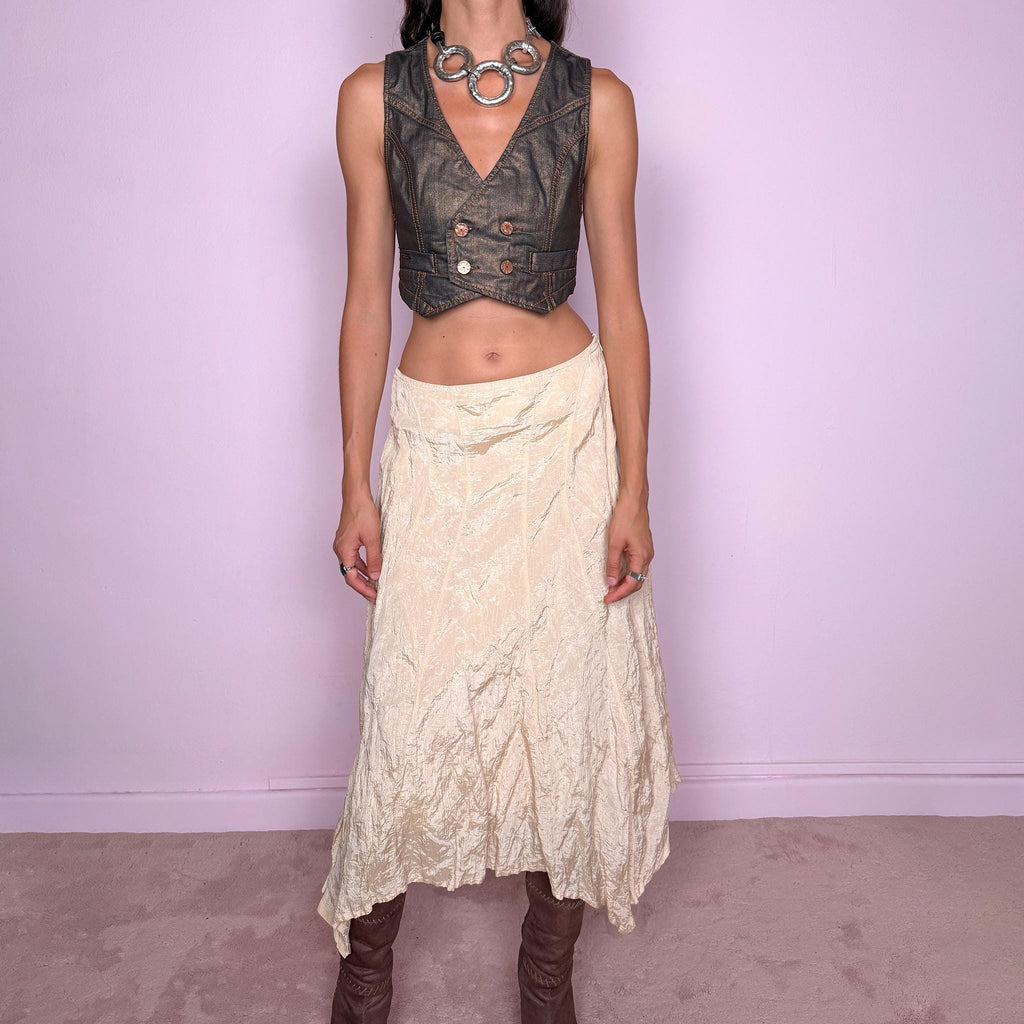 Vintage 2000s light cream-gold asymmetric midi skirt featuring a flared silhouette with an irregular handkerchief-style hem and a subtly crinkled, textured finish. Crafted from a structured, non-stretch blend of 53% polyamide, 32% cotton and 15% metallic fiber, with a 65% acetate and 35% viscose lining. Finished with a side zip closure. Can be worn mid-rise for size S or lower on the waist for size XS. From a German brand. Excellent vintage condition.