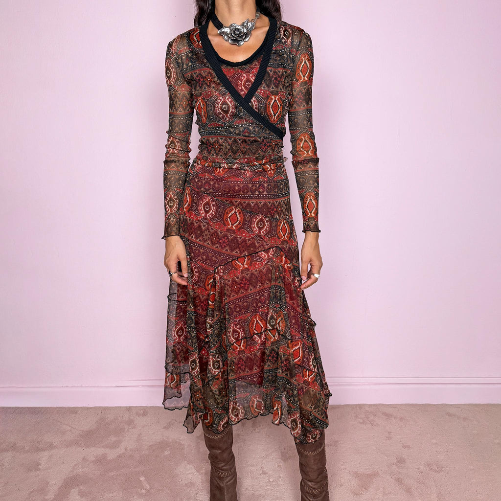 Vintage 2000s printed mesh two-piece dress set. The set includes a fitted sleeveless midi dress with a red lining and asymmetric layered hem, paired with a long-sleeve sheer mesh wrap top with tie fastening and contrasting black trim. Finished in an earthy red, burgundy, brown, and orange graphic print throughout. Perfect for layered bohemian styling. From a French brand, made in France from stretchy 100% polyester. Great vintage condition.