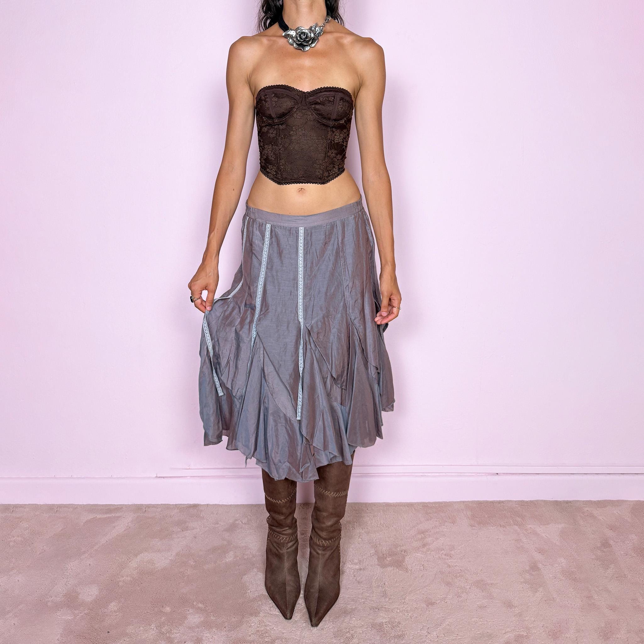 Vintage 2000s bluish-gray iridescent midi skirt featuring a subtle sheen that shifts between dusty blue, gray, and muted mauve tones. Designed with a fluid asymmetric layered construction, curved paneling, delicate lace-trim inserts, and an irregular hem that creates soft movement and a deconstructed silhouette. Perfect for delicate, ethereal styling. Features a back zip closure and no stretch. Can be worn high-waisted for size M or lower-rise for sizes XS–S. Made from 70% cotton and 30% silk