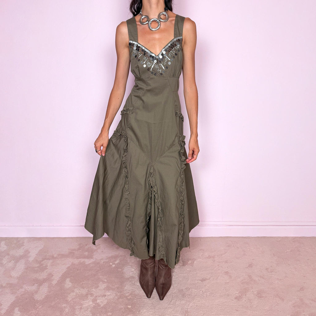 Vintage 2000s khaki green maxi dress crafted from 100% cotton, featuring a fitted empire-waist silhouette, wide shoulder straps, and a softly flared asymmetric hem. The neckline is heavily embellished with metallic silver sequins and beading arranged in a statement geometric pattern, contrasting with the earthy cotton fabric. Finished with sculptural panel construction and delicate ruffled trim running along the skirt seams.