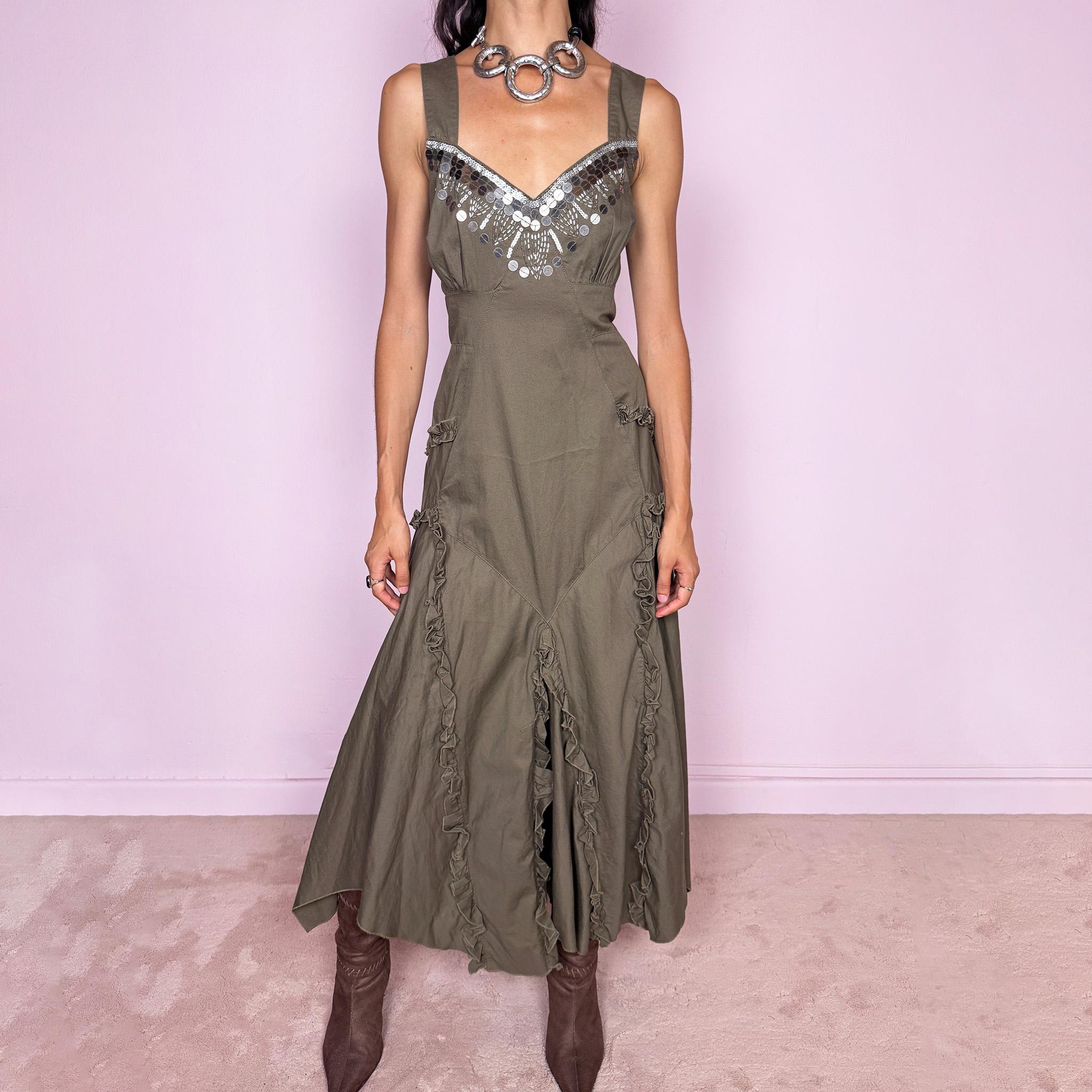 Vintage 2000s khaki green maxi dress crafted from 100% cotton, featuring a fitted empire-waist silhouette, wide shoulder straps, and a softly flared asymmetric hem. The neckline is heavily embellished with metallic silver sequins and beading arranged in a statement geometric pattern, contrasting with the earthy cotton fabric. Finished with sculptural panel construction and delicate ruffled trim running along the skirt seams.