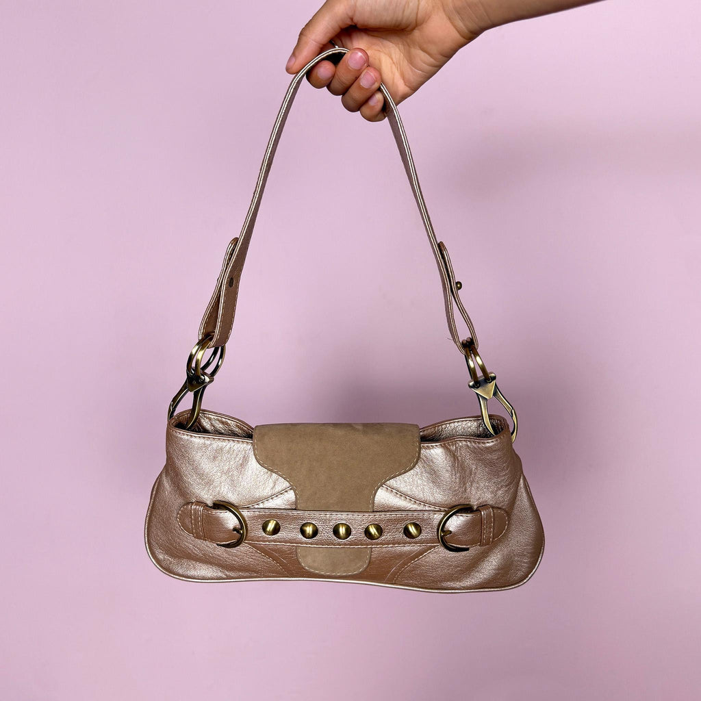 Vintage 2000s shoulder bag made in Italy in a beautiful metallic bronze-taupe shade with warm golden undertones. Designed with a baguette silhouette, statement buckle-inspired front detailing with antique brass-tone hardware, a shoulder strap, and a suede front flap. Finished with a zip-top closure. The interior label states "Genuine Leather". Excellent vintage condition.