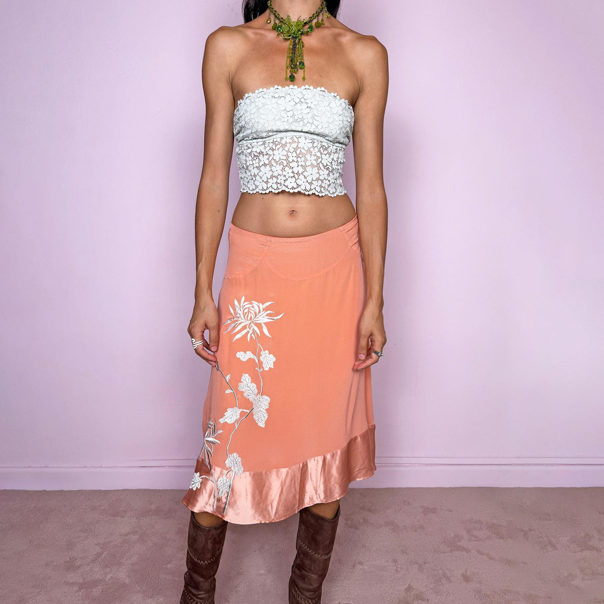 Vintage 2000s pastel salmon-orange midi skirt crafted from a fluid, non-stretch fabric with a silk-like feel, featuring delicate white floral embroidery, a flared silhouette, satin trim at the hem, and a satin lining. The soft salmon tone and botanical embroidery give it a dreamy, romantic bohemian aesthetic. The composition label is missing, so the exact fabric is unknown, though it has the look and feel of silk. From a Danish brand.