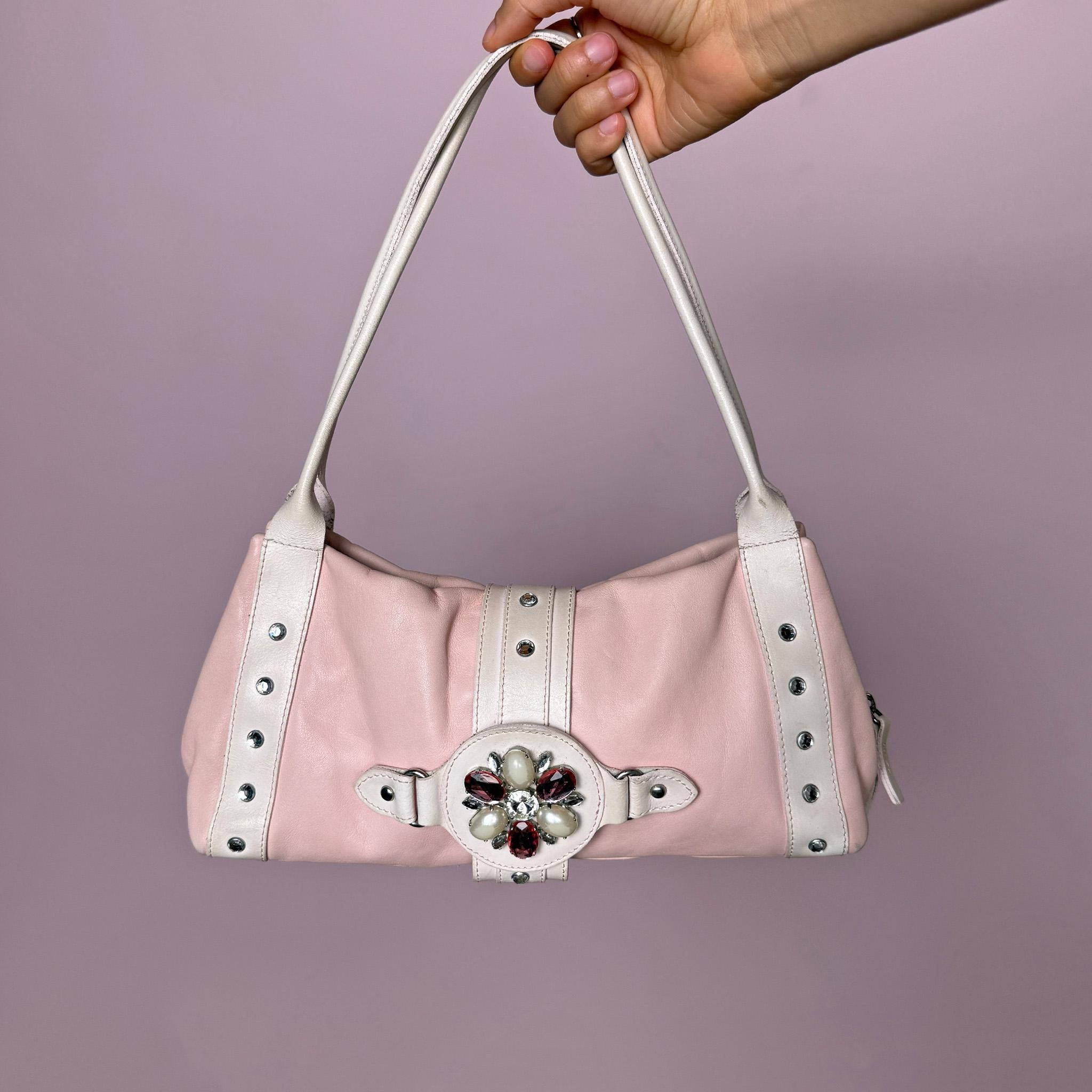 Vintage 2000s Montini pink genuine leather shoulder bag. Features a soft Y2K baguette-inspired silhouette, full top zip closure, magnetic snap button closure, white leather shoulder straps, silver-tone stud details, and a decorative jeweled front strap with faux pearl and pink rhinestone accents. Compact yet eye-catching, with a soft, feminine, and playful 2000s rococo coquette aesthetic. Made in Italy.