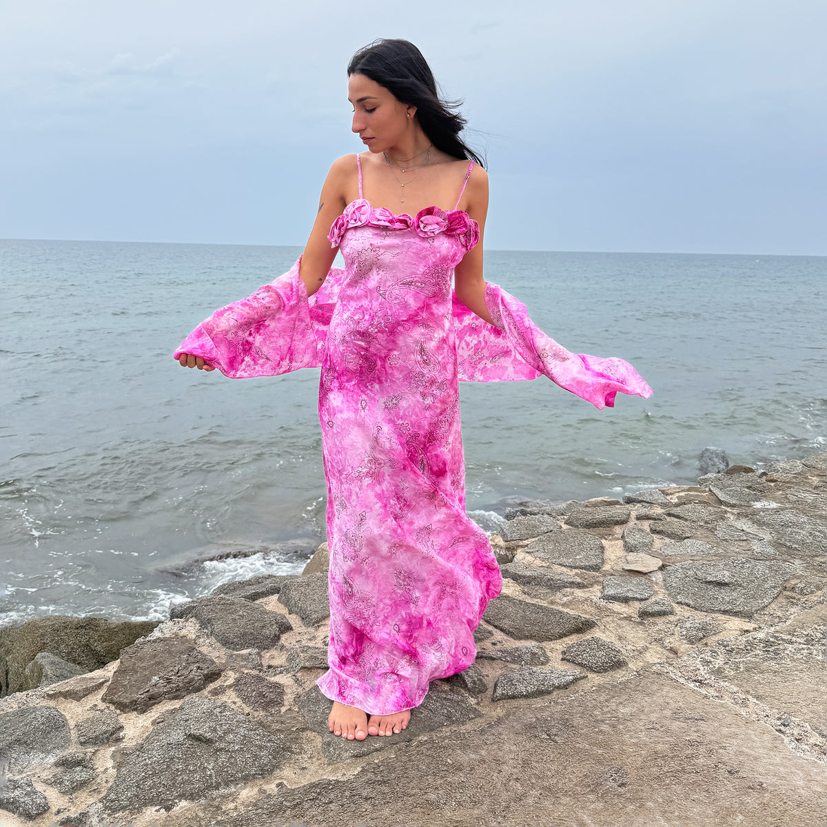 Vintage 2000s pink slip maxi dress from a French brand, made in France. Features a vivid pink tie-dye paisley print, slim spaghetti straps, rosette appliqué detailing along the neckline, and a long bias-cut silhouette with a flared hem. Comes with a matching scarf for versatile styling. Perfect for romantic occasionwear, summer evening looks, and statement formal styling. Made from a non-stretch blend of 71% viscose and 29% polyester with a 100% polyester lining. Excellent vintage condition.