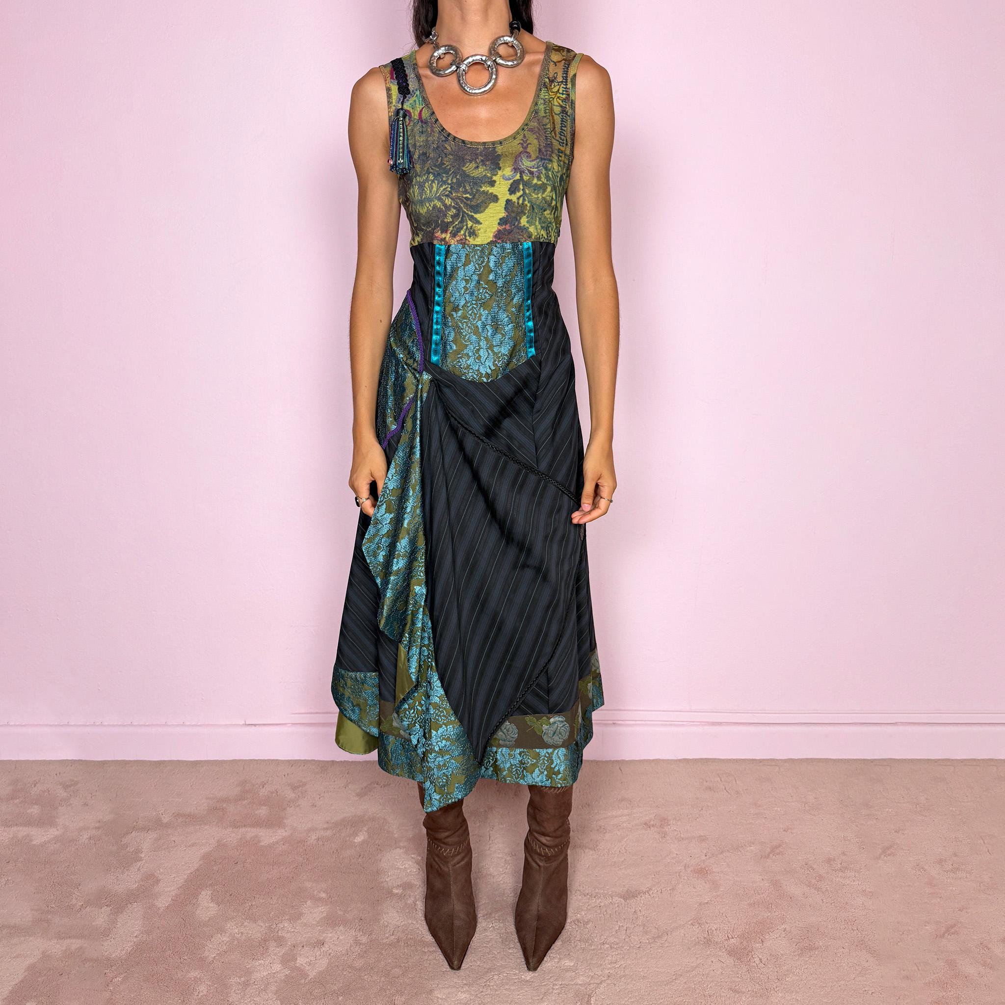 Vintage 2000s midi dress designed with a dramatic, medieval-inspired avant-garde silhouette. It features a graphic bust panel with green multicolored abstract artwork, a fitted waist with blue lace panels, a side zip closure, and a flowing asymmetric skirt with mixed striped fabrics, contrast trims, and layered draped sections that create sculptural movement. A rare fantasy statement piece with a theatrical baroque feel.