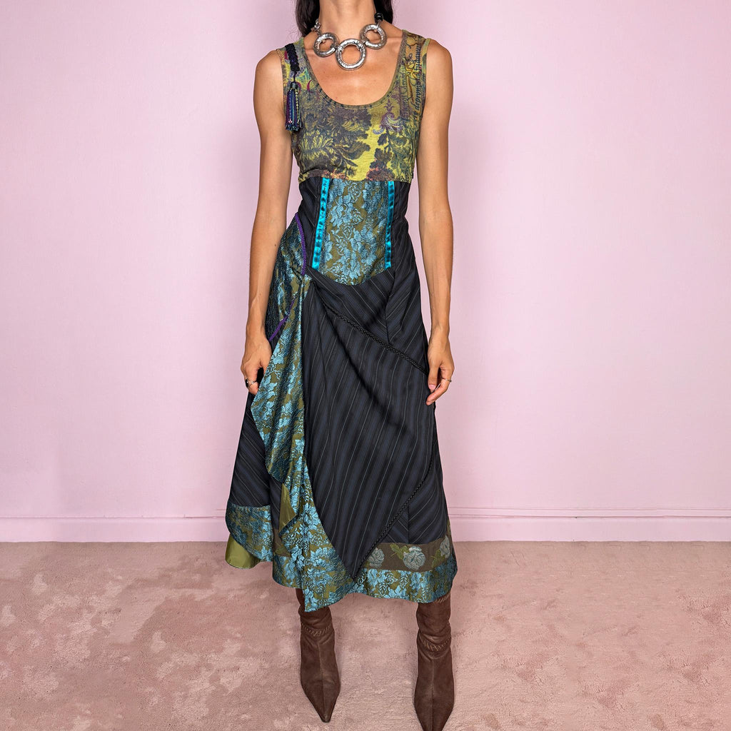 Vintage 2000s midi dress designed with a dramatic, medieval-inspired avant-garde silhouette. It features a graphic bust panel with green multicolored abstract artwork, a fitted waist with blue lace panels, a side zip closure, and a flowing asymmetric skirt with mixed striped fabrics, contrast trims, and layered draped sections that create sculptural movement. A rare fantasy statement piece with a theatrical baroque feel.
