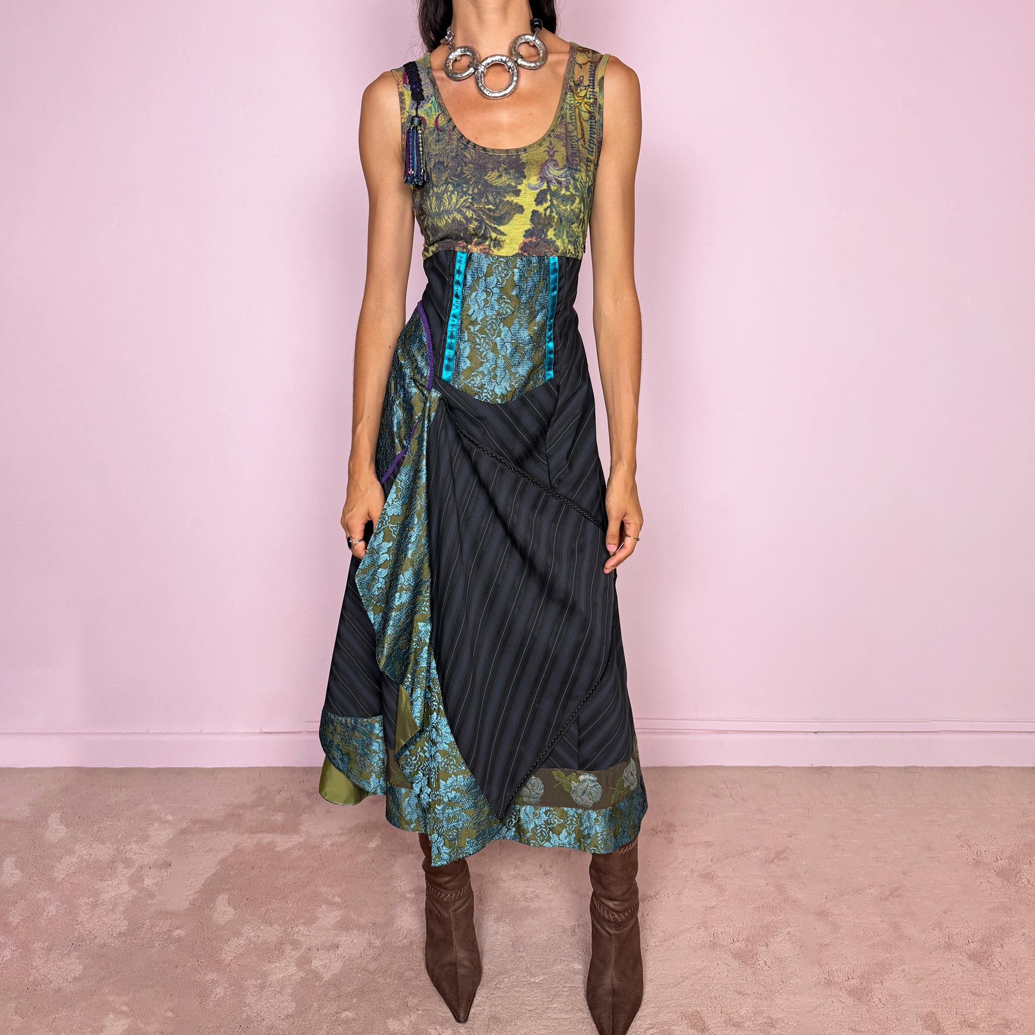 Vintage 2000s midi dress designed with a dramatic, medieval-inspired avant-garde silhouette. It features a graphic bust panel with green multicolored abstract artwork, a fitted waist with blue lace panels, a side zip closure, and a flowing asymmetric skirt with mixed striped fabrics, contrast trims, and layered draped sections that create sculptural movement. A rare fantasy statement piece with a theatrical baroque feel.
