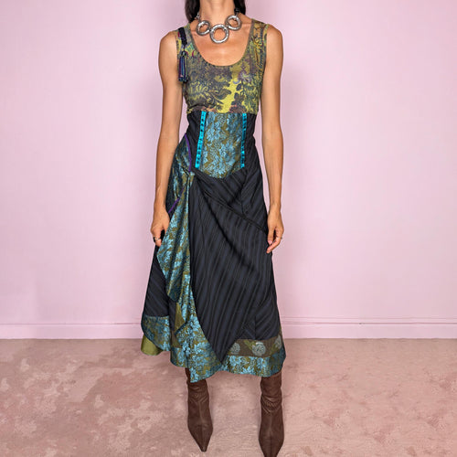 Vintage 2000s midi dress designed with a dramatic, medieval-inspired avant-garde silhouette. It features a graphic bust panel with green multicolored abstract artwork, a fitted waist with blue lace panels, a side zip closure, and a flowing asymmetric skirt with mixed striped fabrics, contrast trims, and layered draped sections that create sculptural movement. A rare fantasy statement piece with a theatrical baroque feel.