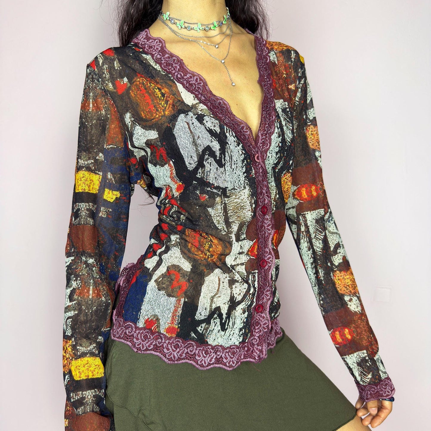 The vintage 2000s mesh sheer blouse features an abstract painting print in burnt orange, ochre, red, and charcoal. Made of stretch polyester mesh, it has long sleeves, a deep V-neckline trimmed in plum lace, and a tonal button front. This top is a rare avant garde piece with a romantic, artsy edge—perfect for chic events, layering, and transitional weather. Excellent vintage condition.