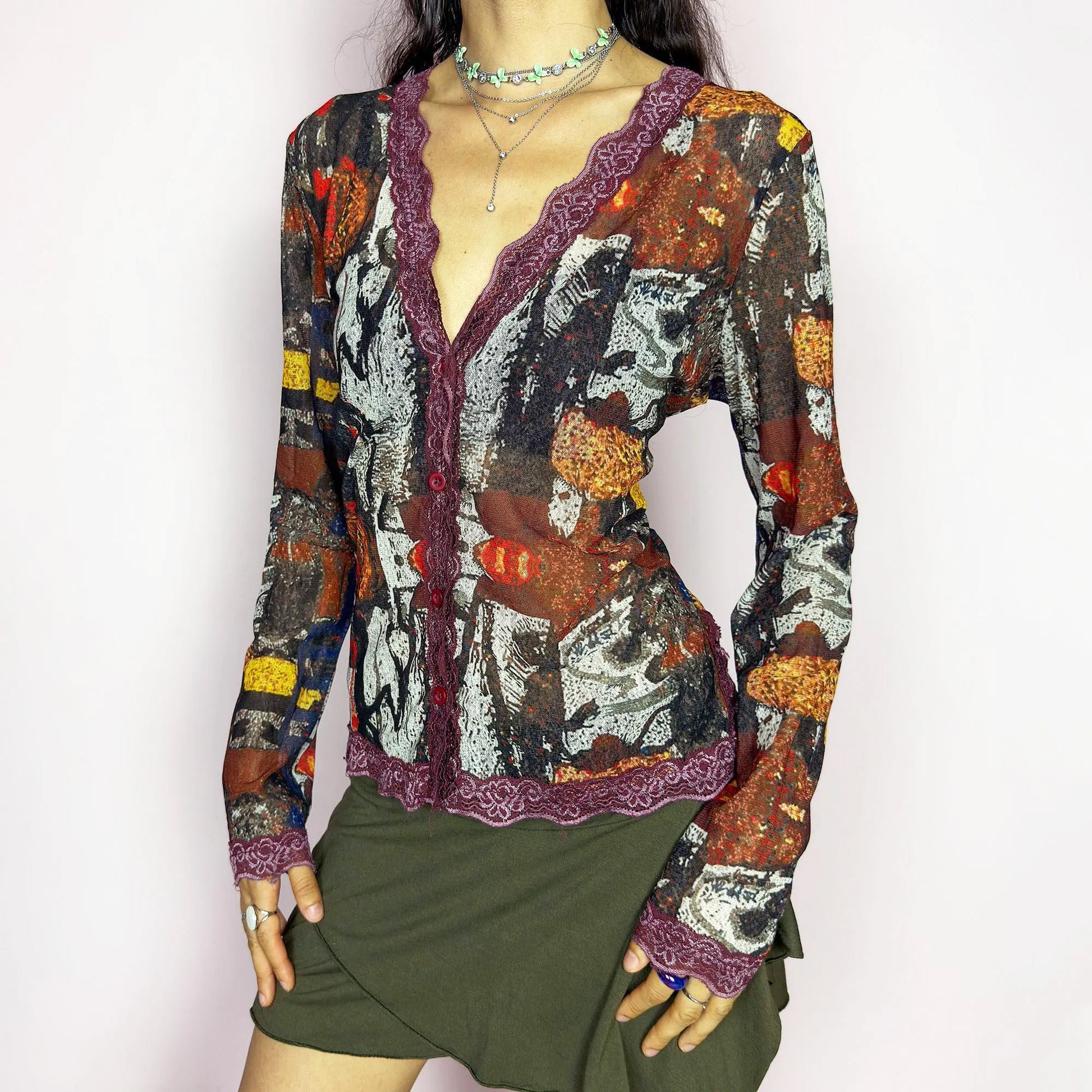 The vintage 2000s mesh sheer blouse features an abstract painting print in burnt orange, ochre, red, and charcoal. Made of stretch polyester mesh, it has long sleeves, a deep V-neckline trimmed in plum lace, and a tonal button front. This top is a rare avant garde piece with a romantic, artsy edge, perfect for chic events, layering, and transitional weather. Excellent vintage condition.