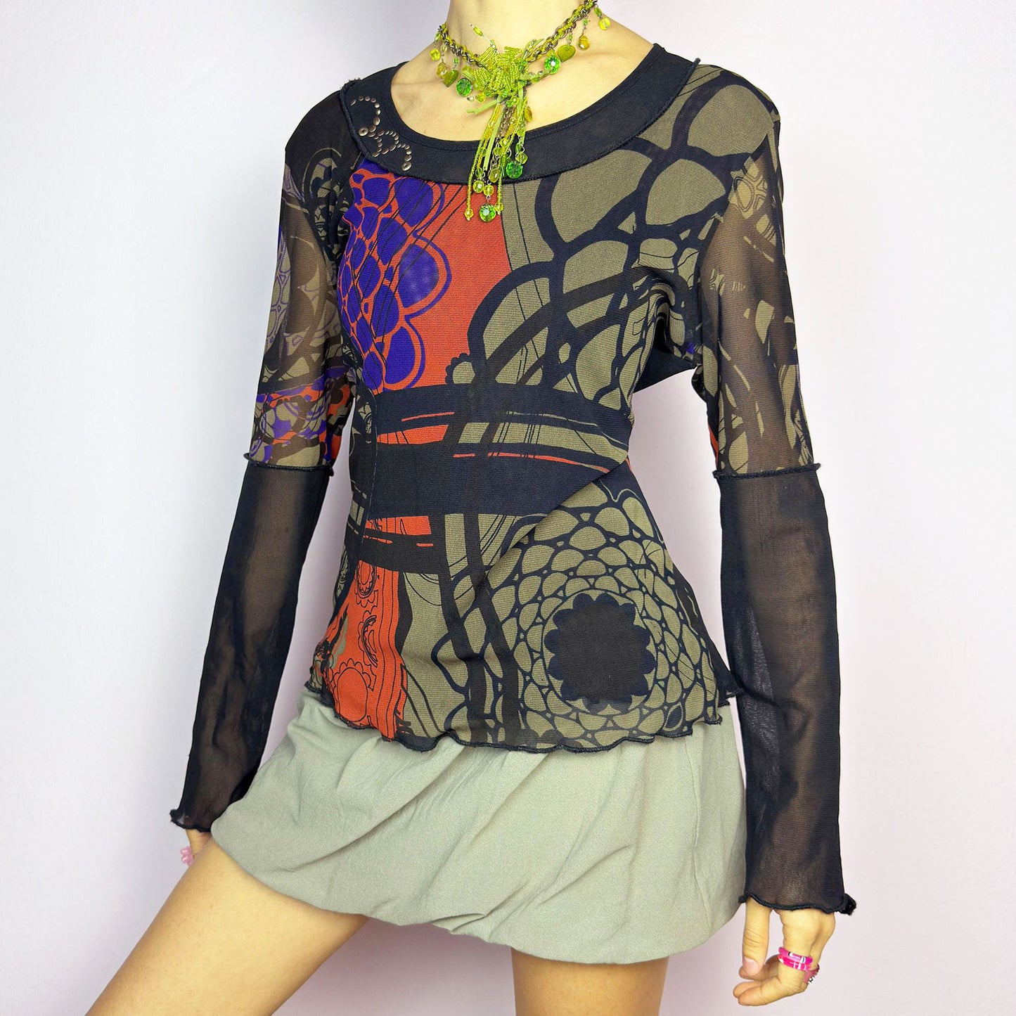 The Y2K Abstract Printed Mesh Top is a vintage 2000s sheer long-sleeve top featuring a bold abstract print in earthy tones with pops of red and blue. Designed with contrast black mesh sleeves, this artistic piece is perfect for edgy streetwear, cyberpunk, or grunge-inspired outfits. Ideal for layering or wearing solo for a statement look.