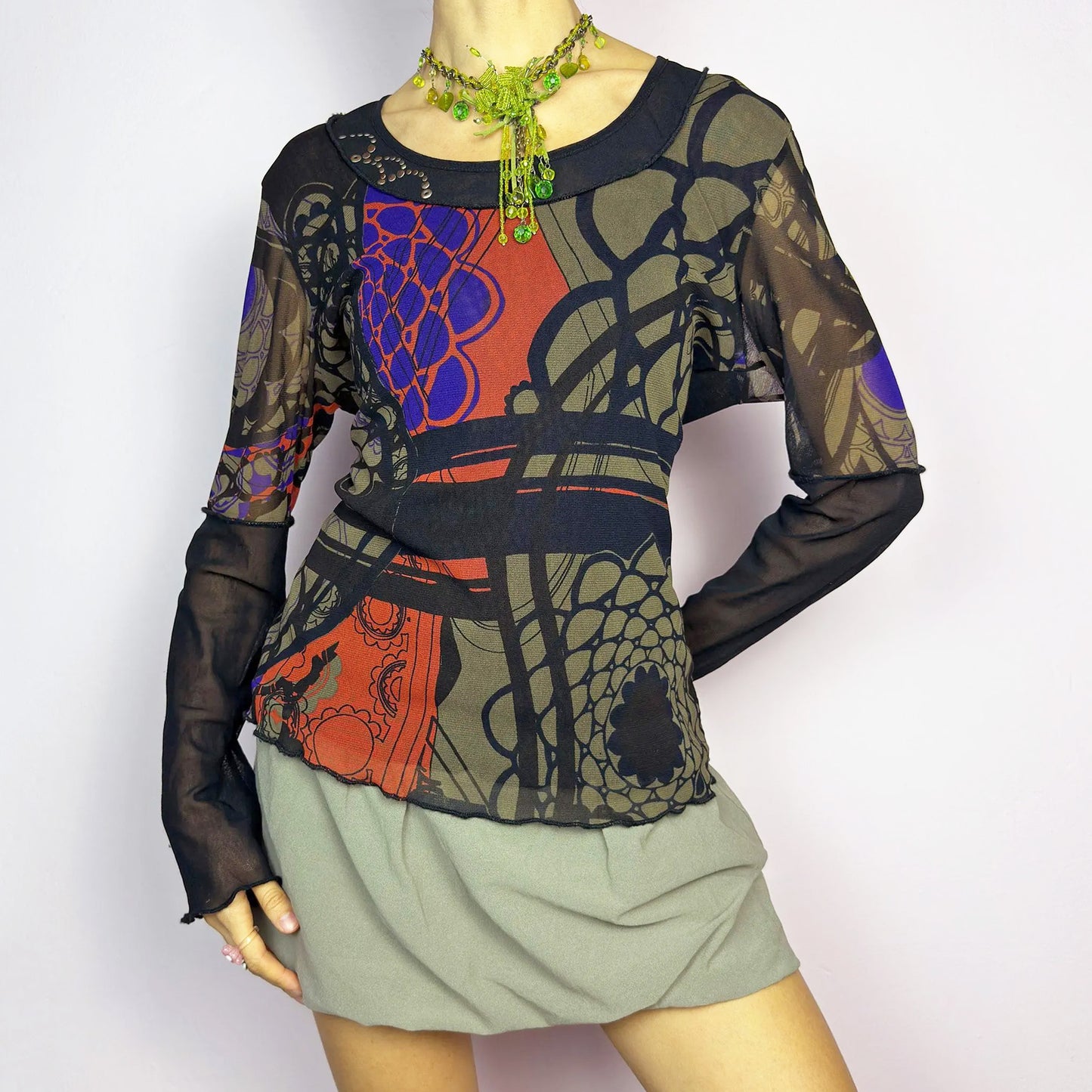 The Y2K Abstract Printed Mesh Top is a vintage 2000s sheer long-sleeve top featuring a bold abstract print in earthy tones with pops of red and blue. Designed with contrast black mesh sleeves, this artistic piece is perfect for edgy streetwear, cyberpunk, or grunge-inspired outfits. Ideal for layering or wearing solo for a statement look. Excellent vintage condition.