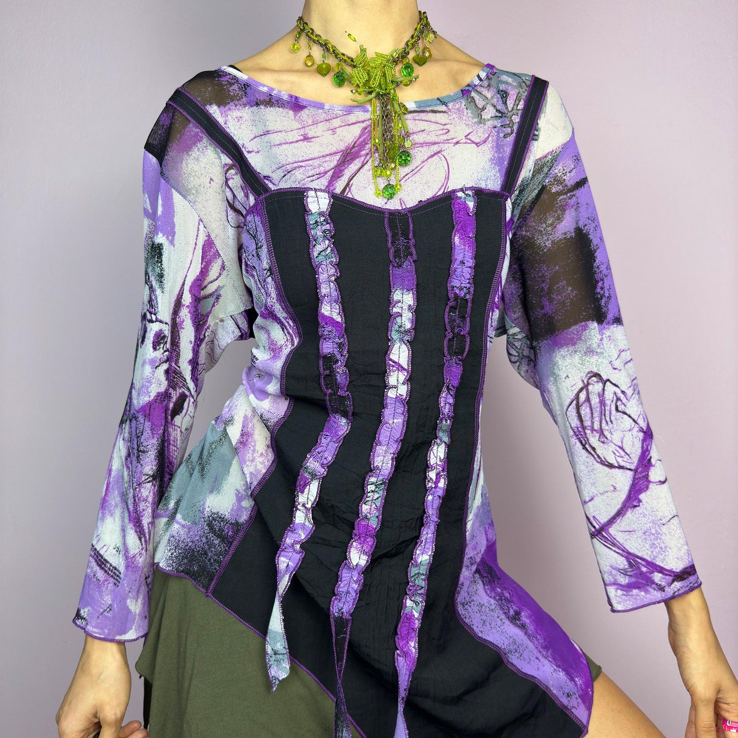 The Y2K Mesh Asymmetric Black Top is a vintage 2000s piece featuring a semi-sheer mesh fabric with an abstract purple, black, and white print. Designed with three quarter sleeves and contrast paneling and exposed seams, this top has a deconstructed, edgy aesthetic. The asymmetric hem and raw cut details add a unique touch, making it perfect for grunge or fairycore-inspired outfits. Lightweight and stretchy, ideal for layering and statement looks. adult world shop