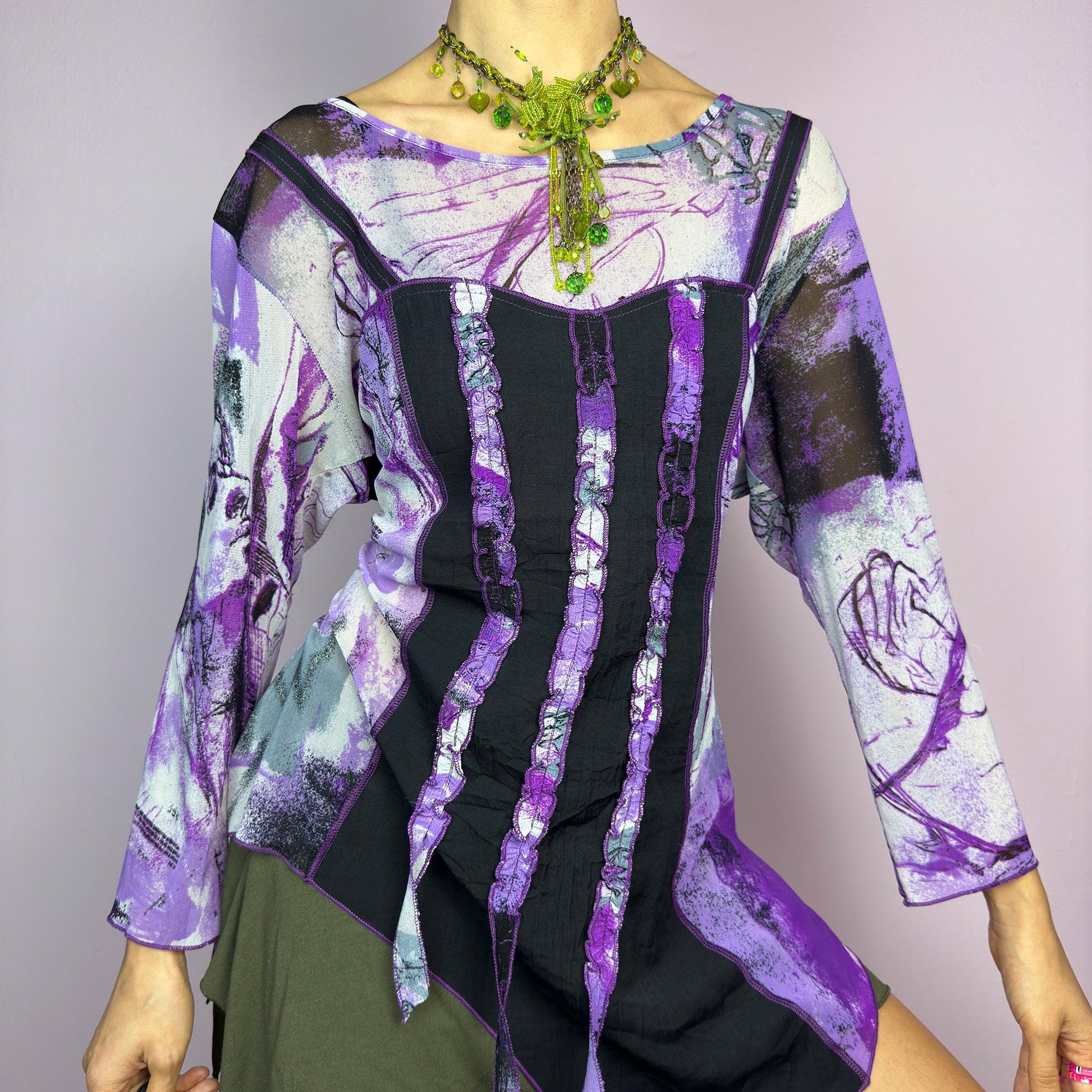 The Y2K Mesh Asymmetric Black Top is a vintage 2000s piece featuring a semi-sheer mesh fabric with an abstract purple, black, and white print. Designed with three quarter sleeves and contrast paneling and exposed seams, this top has a deconstructed, edgy aesthetic. The asymmetric hem and raw cut details add a unique touch, making it perfect for grunge or fairycore-inspired outfits. Lightweight and stretchy, ideal for layering and statement looks. adult world shop