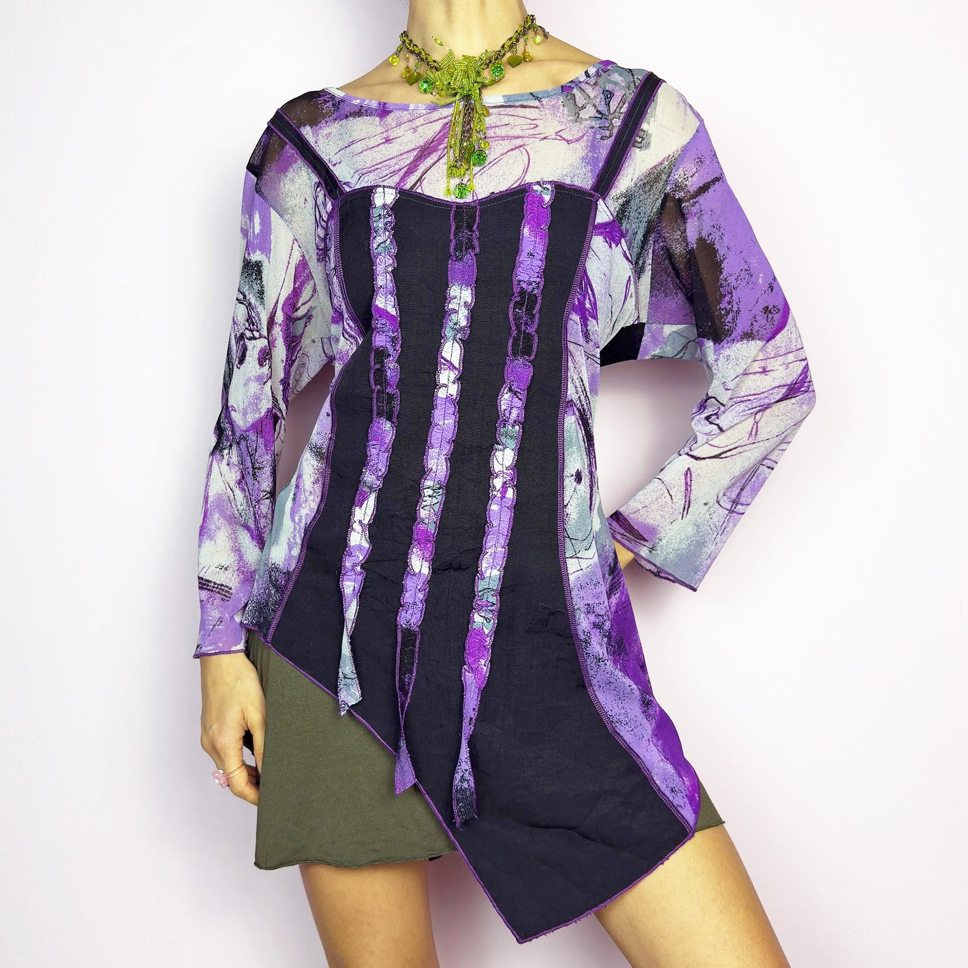 The Y2K Mesh Asymmetric Black Top is a vintage 2000s piece featuring a semi-sheer mesh fabric with an abstract purple, black, and white print. Designed with three quarter sleeves and contrast paneling and exposed seams, this top has a deconstructed, edgy aesthetic. The asymmetric hem and raw cut details add a unique touch, making it perfect for grunge or fairycore-inspired outfits. Lightweight and stretchy, ideal for layering and statement looks. Excellent vintage condition.