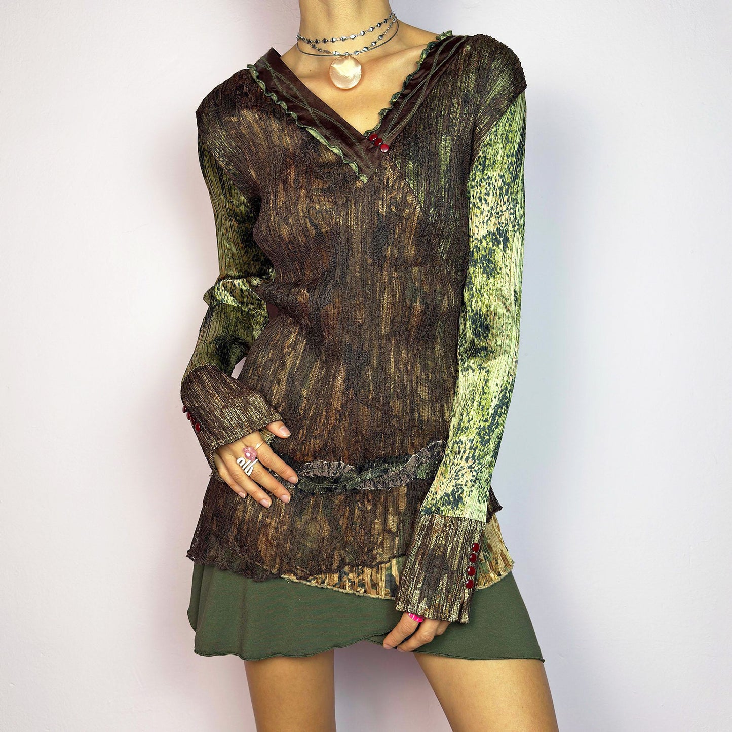 The Y2K Lace Asymmetric Layered Top is a vintage 2000s piece featuring an earthy mix of brown and green tones with a textured, stretchy fabric. This unique top showcases a V-neckline adorned with delicate lace trim, button details, and an asymmetric hemline with layered ruffle accents. The contrasting patchwork design and intricate detailing make it perfect for adding a whimsical and edgy touch to any outfit. Excellent vintage condition.