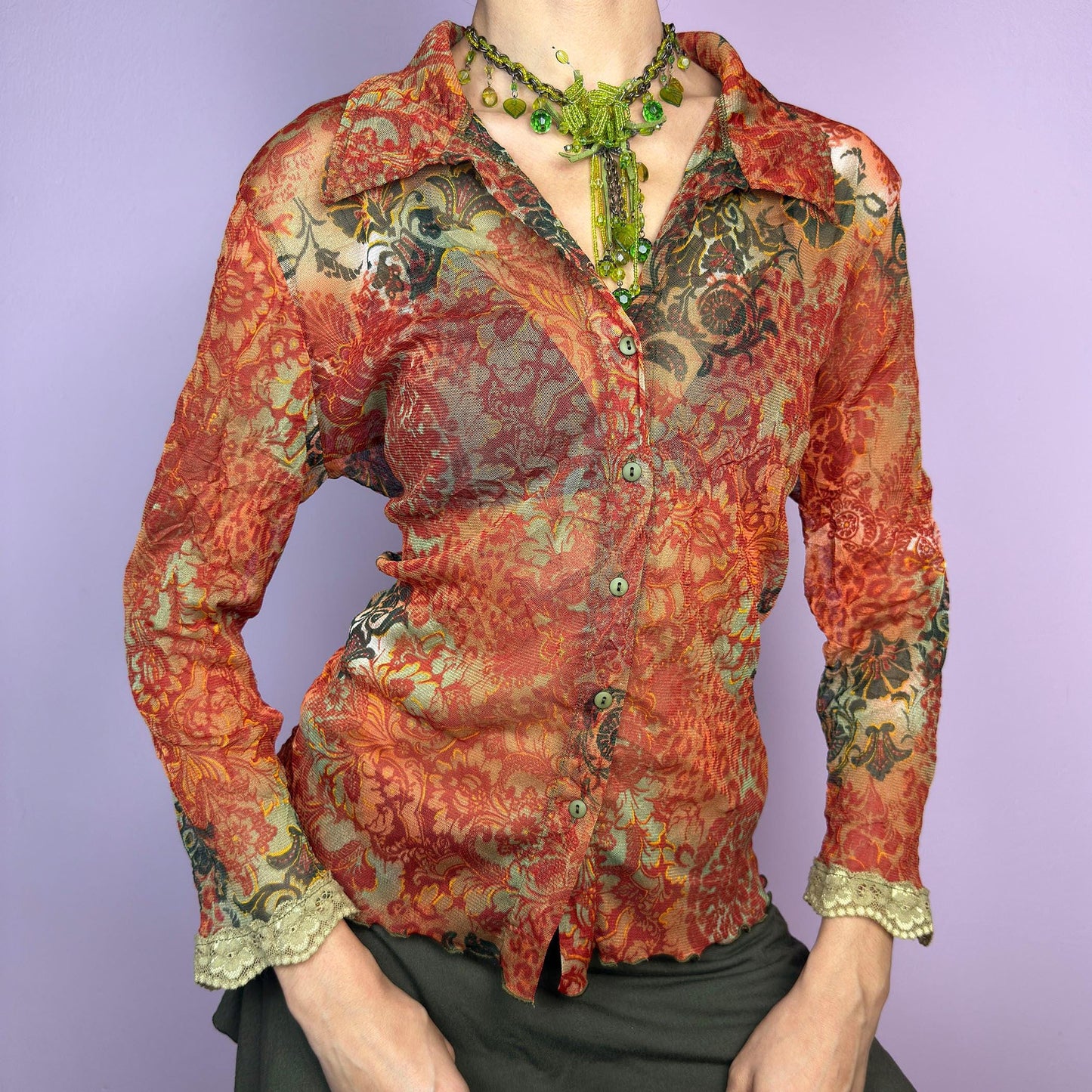 The Y2K Baroque Print Mesh Blouse is a vintage 2000s piece featuring a semi-sheer mesh fabric with a rich baroque-inspired floral print in warm tones. Designed with a fitted silhouette, button-up front, delicate lace trim on the cuffs and three quarter sleeves, the lightweight and stretchy fabric make it ideal for summer bohemian-inspired looks. adult world shop