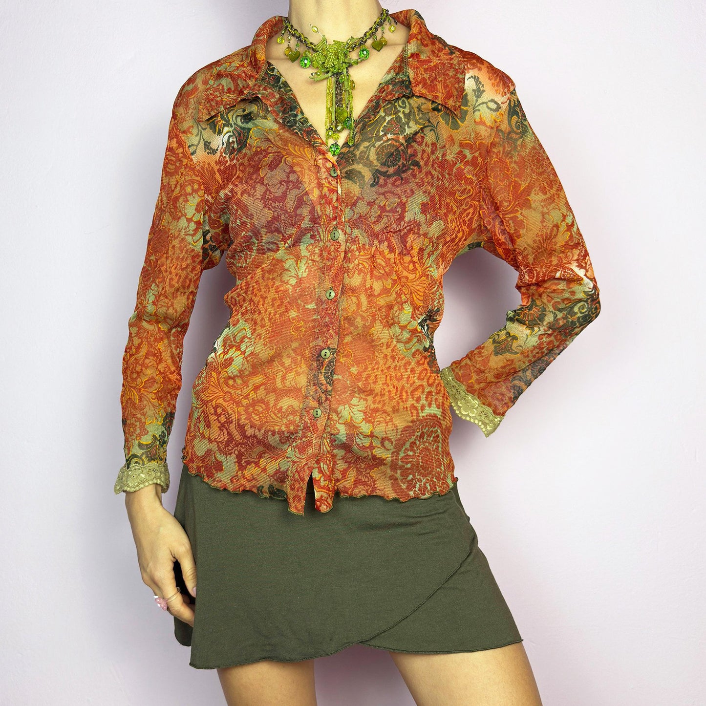 The Y2K Baroque Print Mesh Blouse is a vintage 2000s piece featuring a semi-sheer mesh fabric with a rich baroque-inspired floral print in warm tones. Designed with a fitted silhouette, button-up front, delicate lace trim on the cuffs and three quarter sleeves, the lightweight and stretchy fabric make it ideal for summer bohemian-inspired looks. Excellent vintage condition.