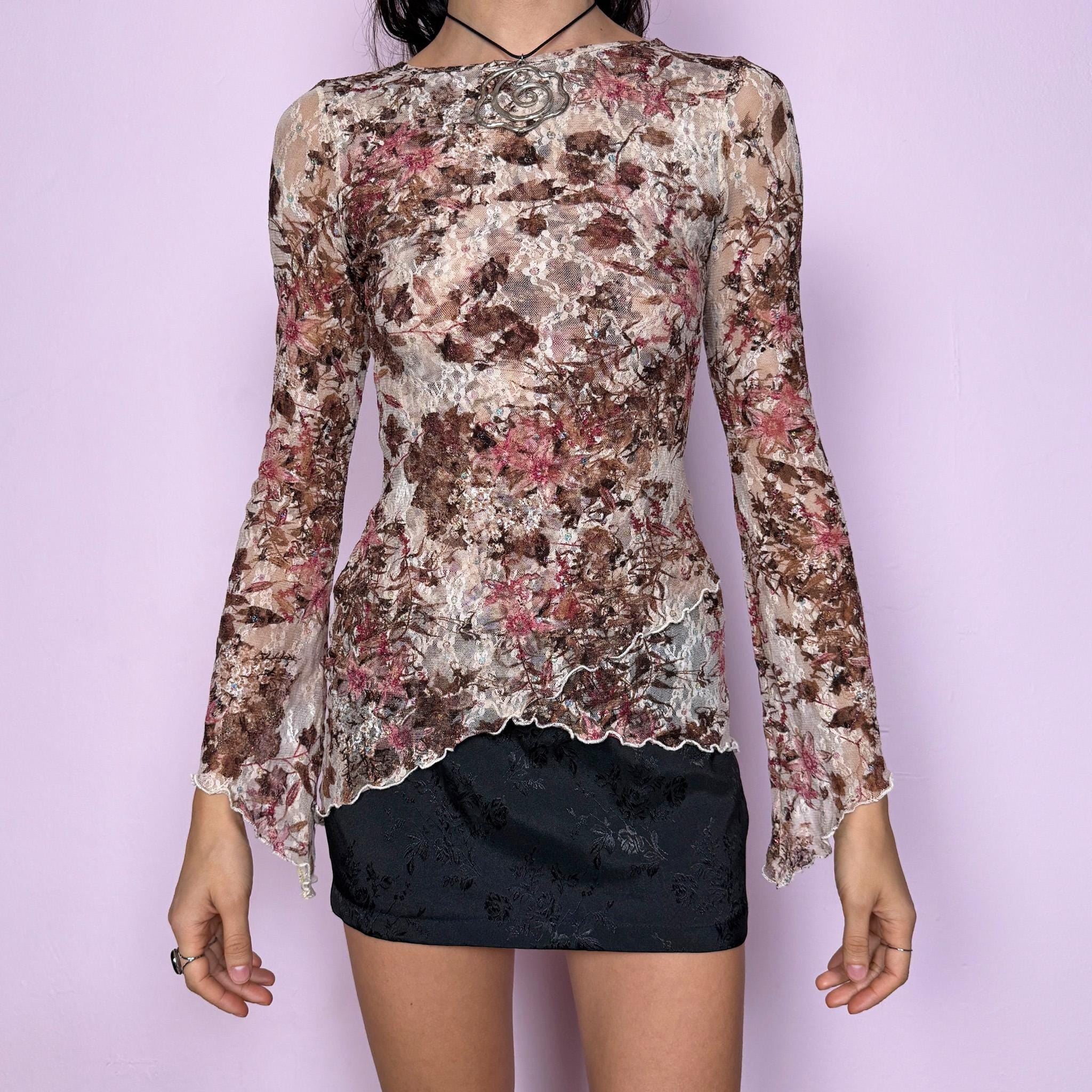 Vintage 2000s beige mesh lace top featuring a romantic brown and maroon floral print with soft glitter accents. Semi-sheer and stretchy with flared sleeves and an asymmetric hem. The fitted silhouette and delicate lace texture create an elegant yet dreamy fairycore aesthetic. Perfect for party nights, boho occasions, or any whimsical and ethereal styling. Excellent vintage condition.
