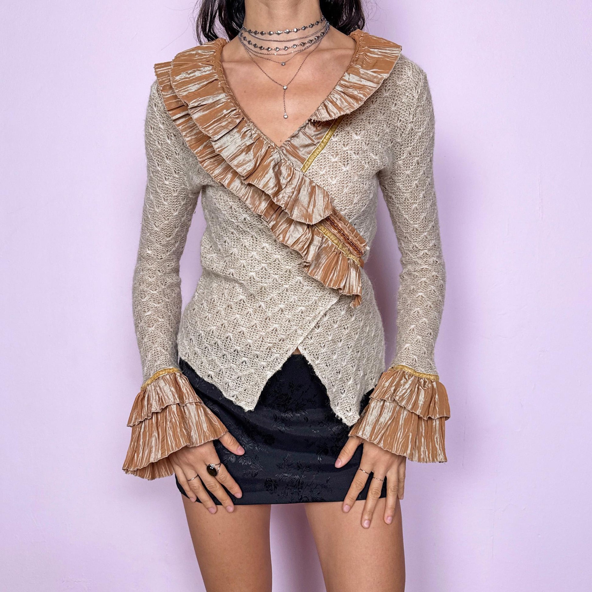 Vintage 2000s beige open-knit wrap cardigan with a dramatic ruffle neckline and tiered mustard-tone ruffle cuffs. Features an elegant tie-back closure, creating a fitted silhouette that highlights the waist. The extravagant design blends romantic, rococo-inspired detailing with a glamorous Y2K formal aesthetic, perfect for event nights, diva moments, or elevated evening styling. Made in France from an acrylic mohair polyester blend. Excellent vintage condition.