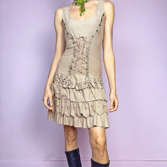 This vintage 2000s mini dress comes in soft beige with a scoop neckline, corset lace-up front, and stretchy fit. The drop waist leads to layered ruffle tiers with eyelet cutouts and scalloped hems. A fairy-meets-western Y2K silhouette—fitted on top, flirty on the bottom. Perfect for casual summer days or standout festival looks. Great vintage condition.
