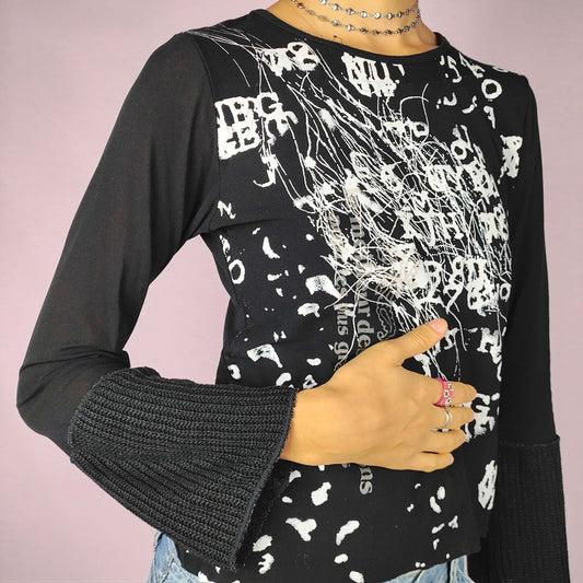 The Y2K Black Printed Top is a vintage 2000s piece with an abstract white graphic print throughout the front. This stretchy top features a sleek black base, flared mesh sleeves, and extended knit cuffs. Ideal for casual wear or a night-out ensemble.
