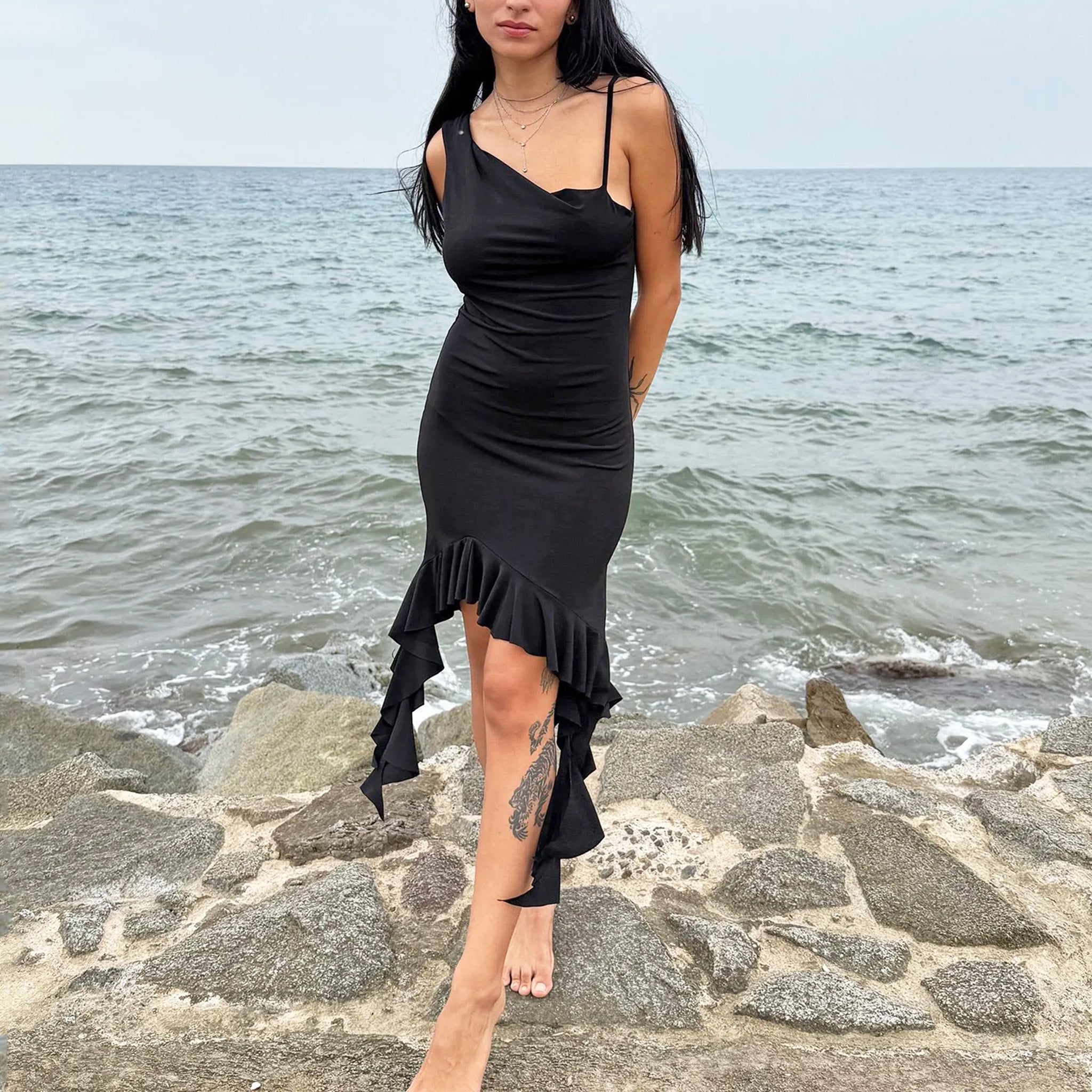 Vintage 2000s black mini dress with asymmetric straps, a subtle cowl neckline, and a dramatic ruffled hem. Stretchy fabric flatters the body with a bold party silhouette, perfect for summer nights, club looks, or diva-inspired Y2K styling. Excellent vintage condition.