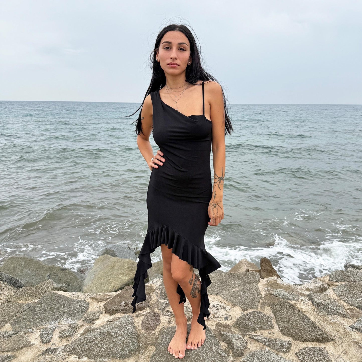 This vintage 2000s black mini dress features asymmetric straps with a subtle cowl neckline and a dramatic ruffled hem. Crafted from a stretchy fabric, it flatters the body with a bold party silhouette. Perfect for summer nights, club looks, or diva-inspired Y2K styling, this piece captures iconic 2000s glamour. Excellent vintage condition.