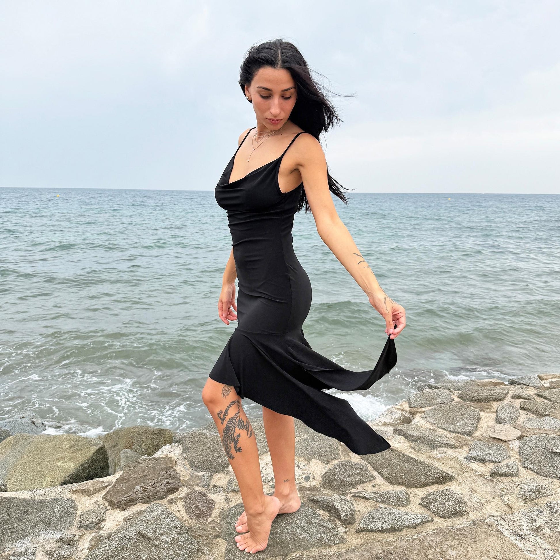 This black vintage 2000s dress features a plunging cowl neckline, and an asymmetrical ruffle hem that flutters with movement. Designed in a flattering cocktail length with a body-hugging silhouette, it’s perfect for summer nights, beach parties, or alt club looks. French-made for a dramatic, femme-fatale feel. An iconic Y2K editorial piece for minimalist seduction. Made from a polyester stretch blend. Great vintage condition.
